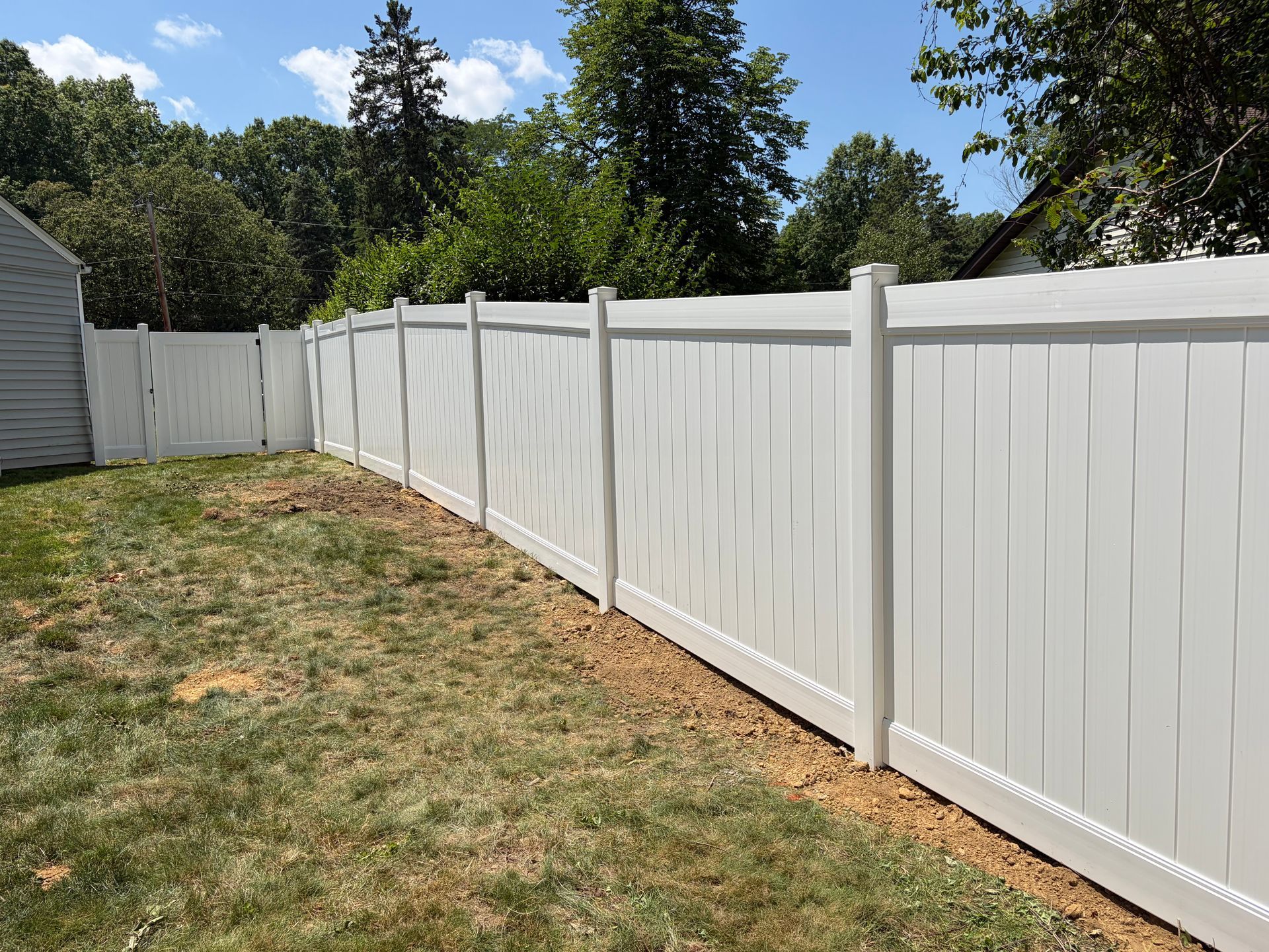White vinyl fence along a grassy backyard with trees and a small shed under a blue sky