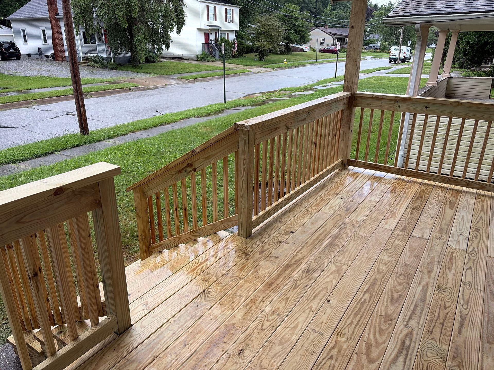 Wooden front porch with wet deck and railing overlooking a quiet residential street