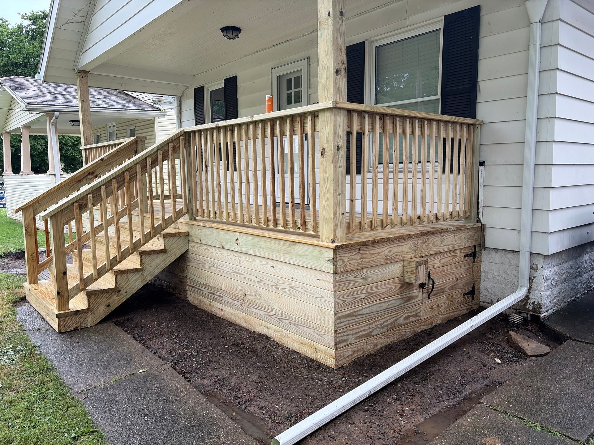Wooden accessibility ramp leading to a house porch, with tan siding and black shutters.