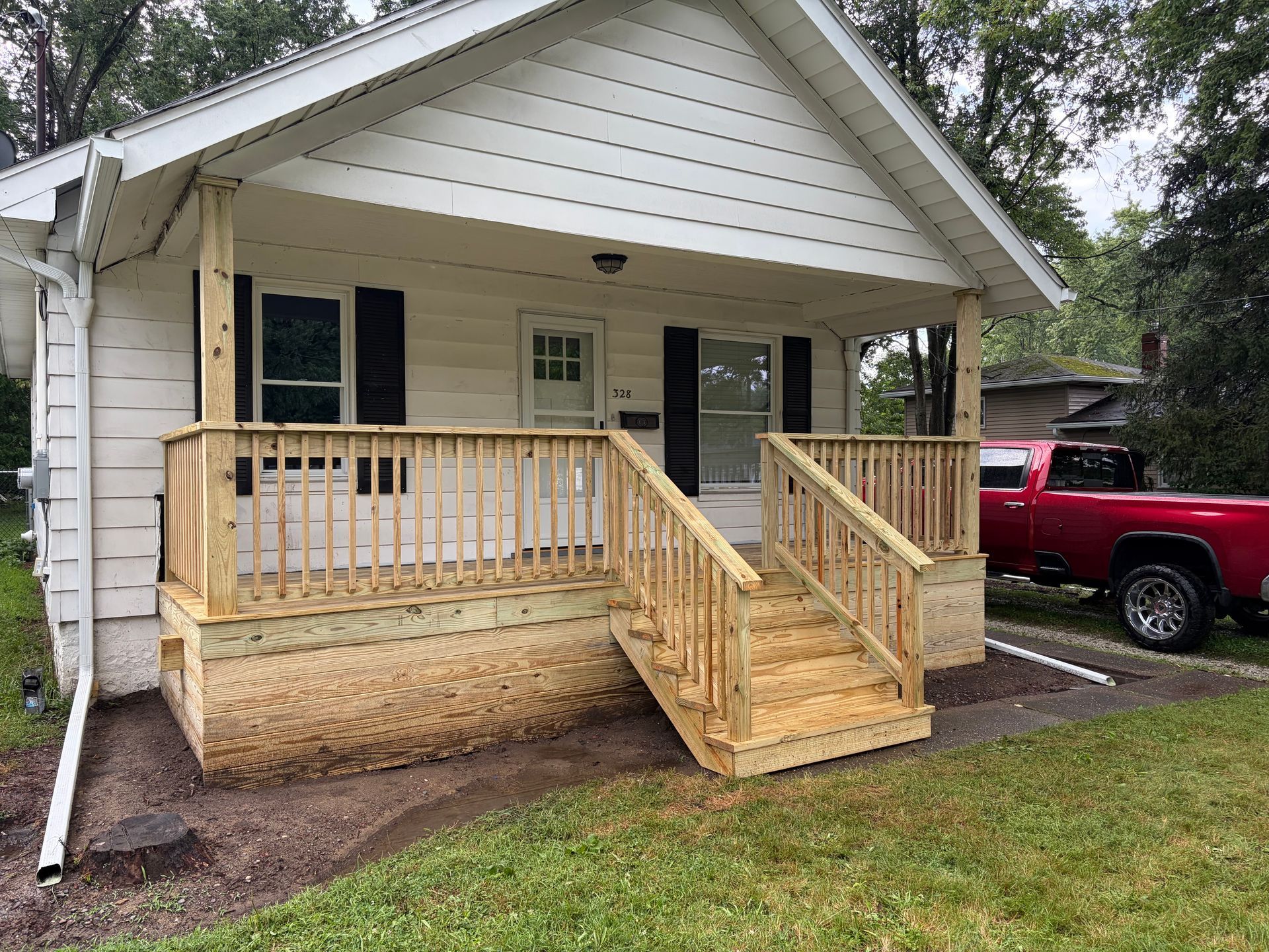 Front porch with wooden accessibility ramp and railing on a white house, red pickup parked nearby.