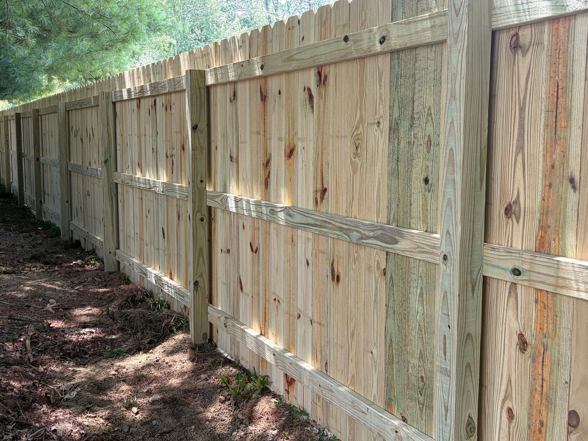 Wooden privacy fence along a wooded path, with sunlight and shadows on the ground