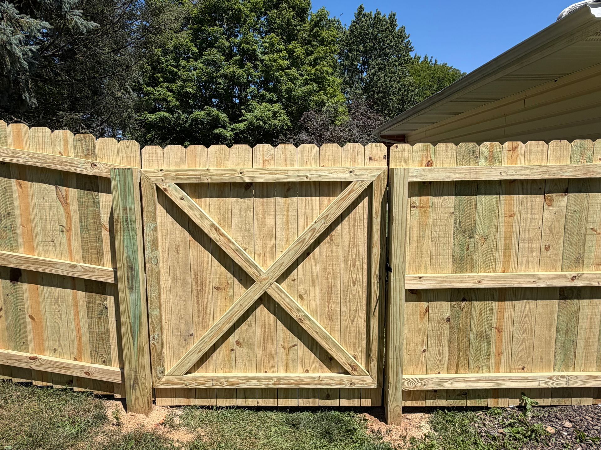 Wooden backyard fence with a central X-braced gate under a sunny sky