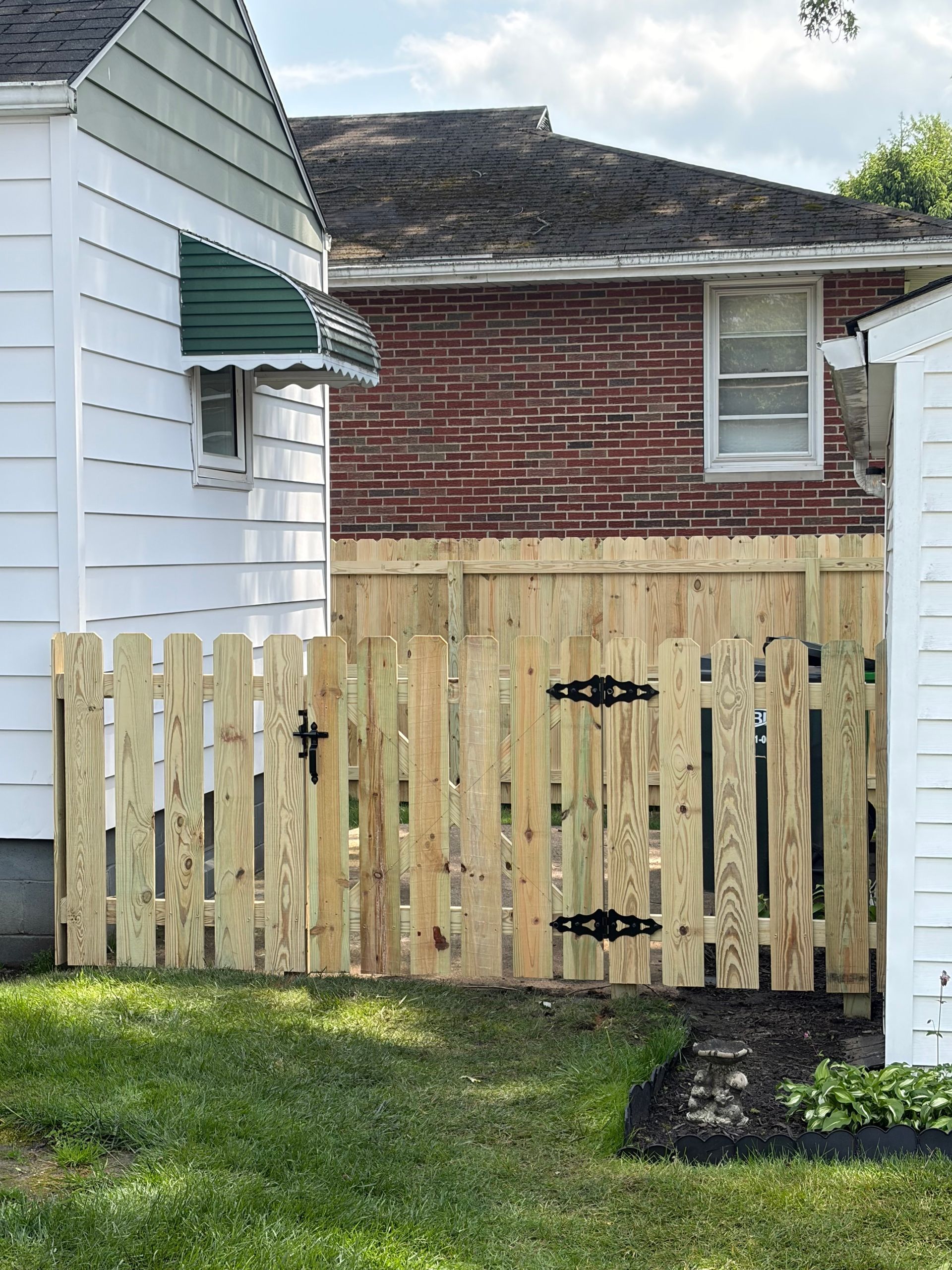 Wooden backyard gate between white and red houses on a grassy lawn