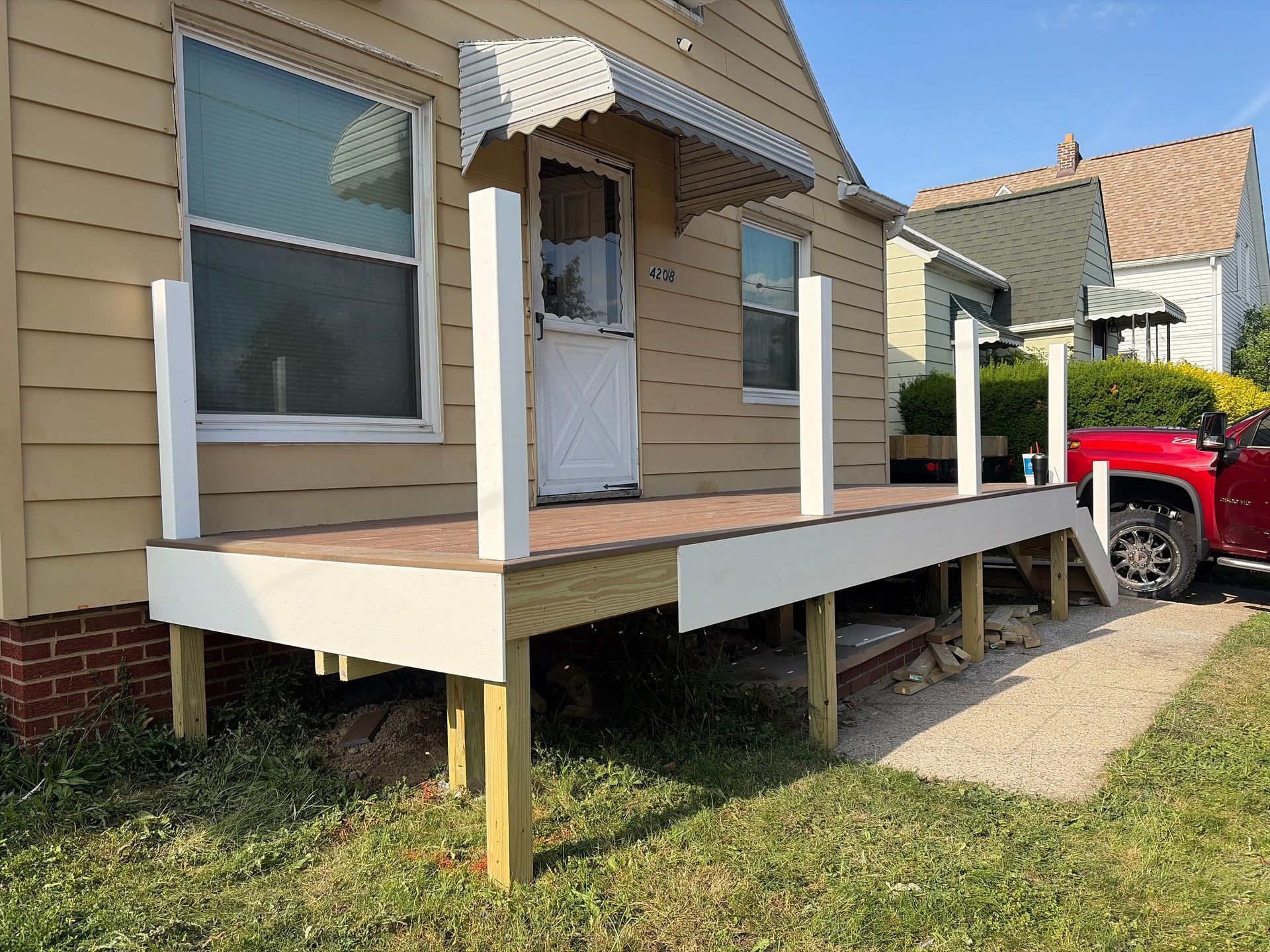 Small tan house with a raised wooden porch and white awning, beside a red pickup truck.