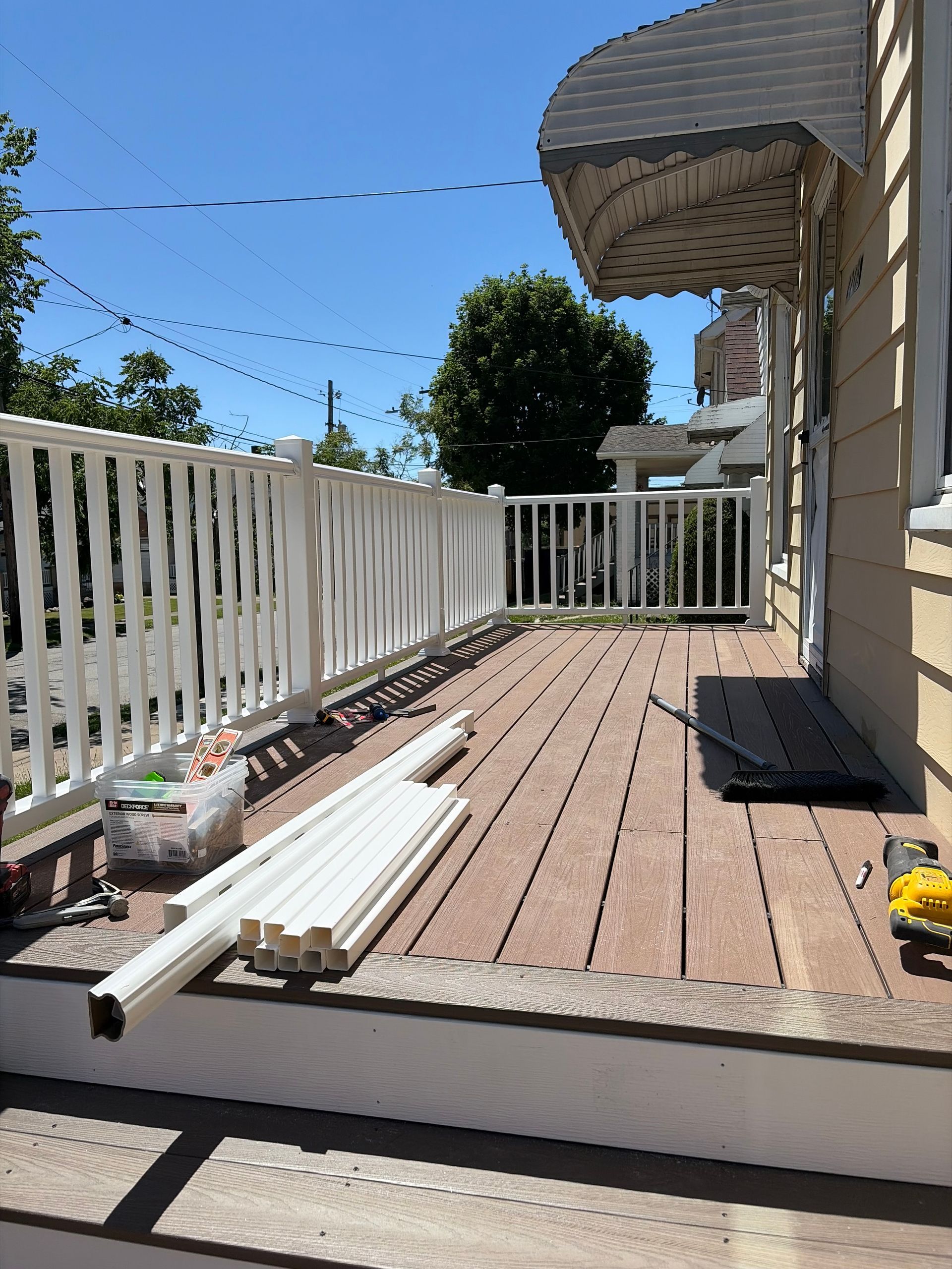 Wooden deck with white railing, coiled hose, and siding on a sunny day