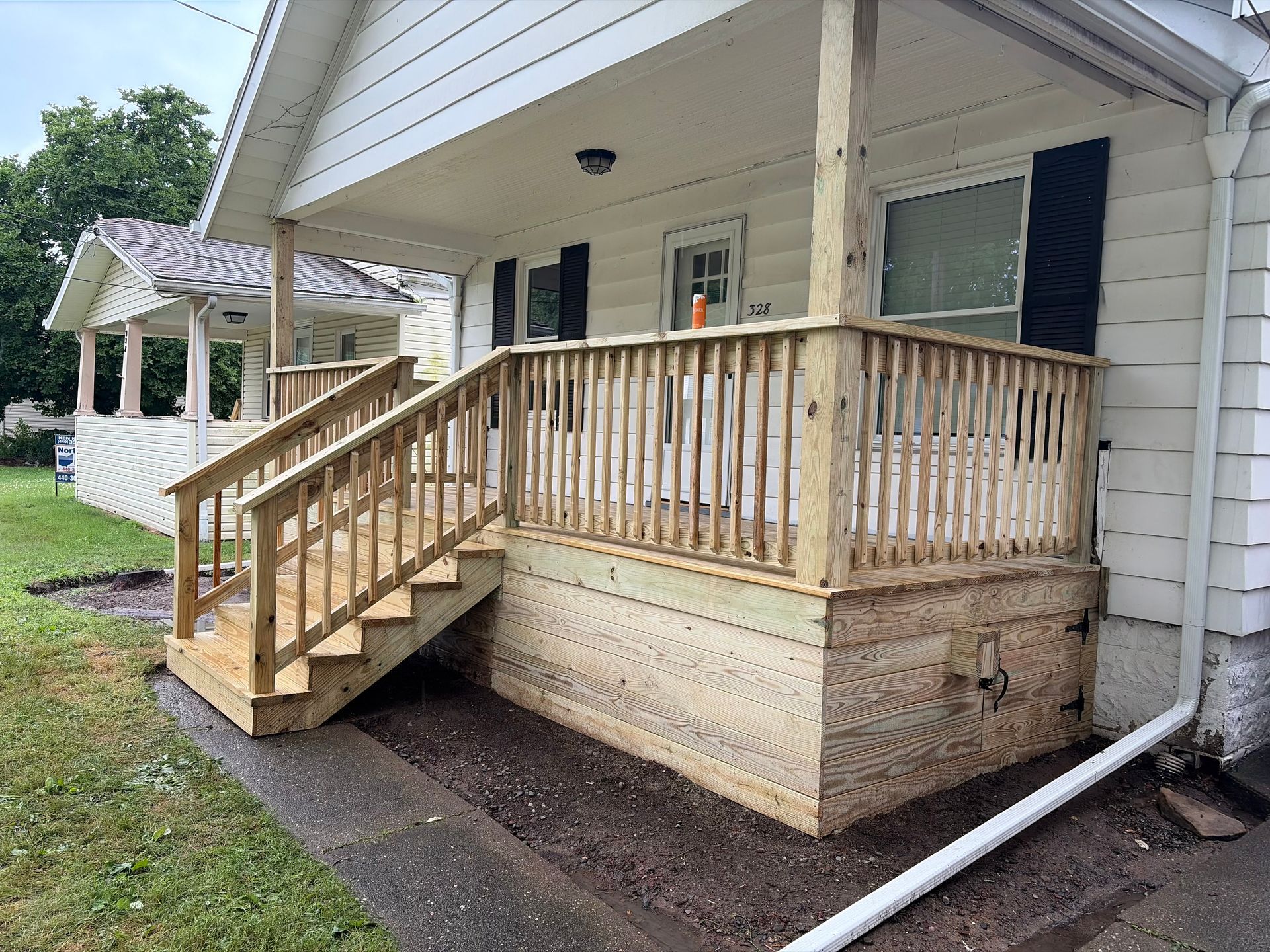 White house porch with wooden steps and railing, screened door, and concrete foundation on a rainy day
