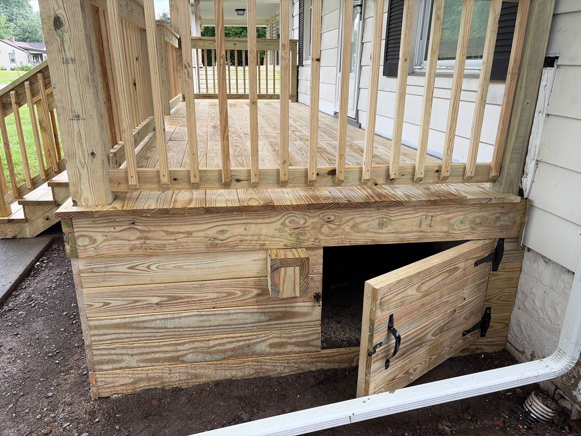 Wooden porch with a small open access door in the skirting, beside a white downspout.