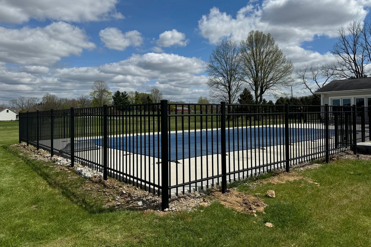 Black metal fence surrounding a blue-covered pool in a grassy yard on a sunny day.