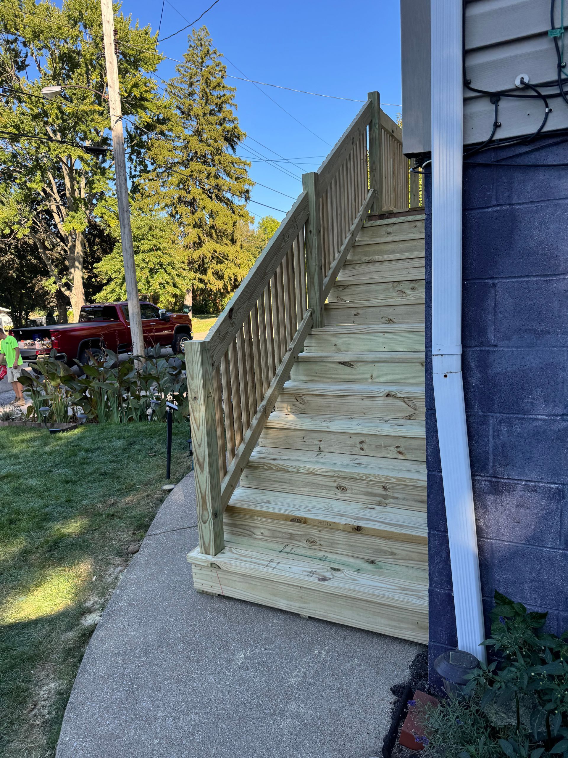 Wooden outdoor stairs with handrails against a blue building.