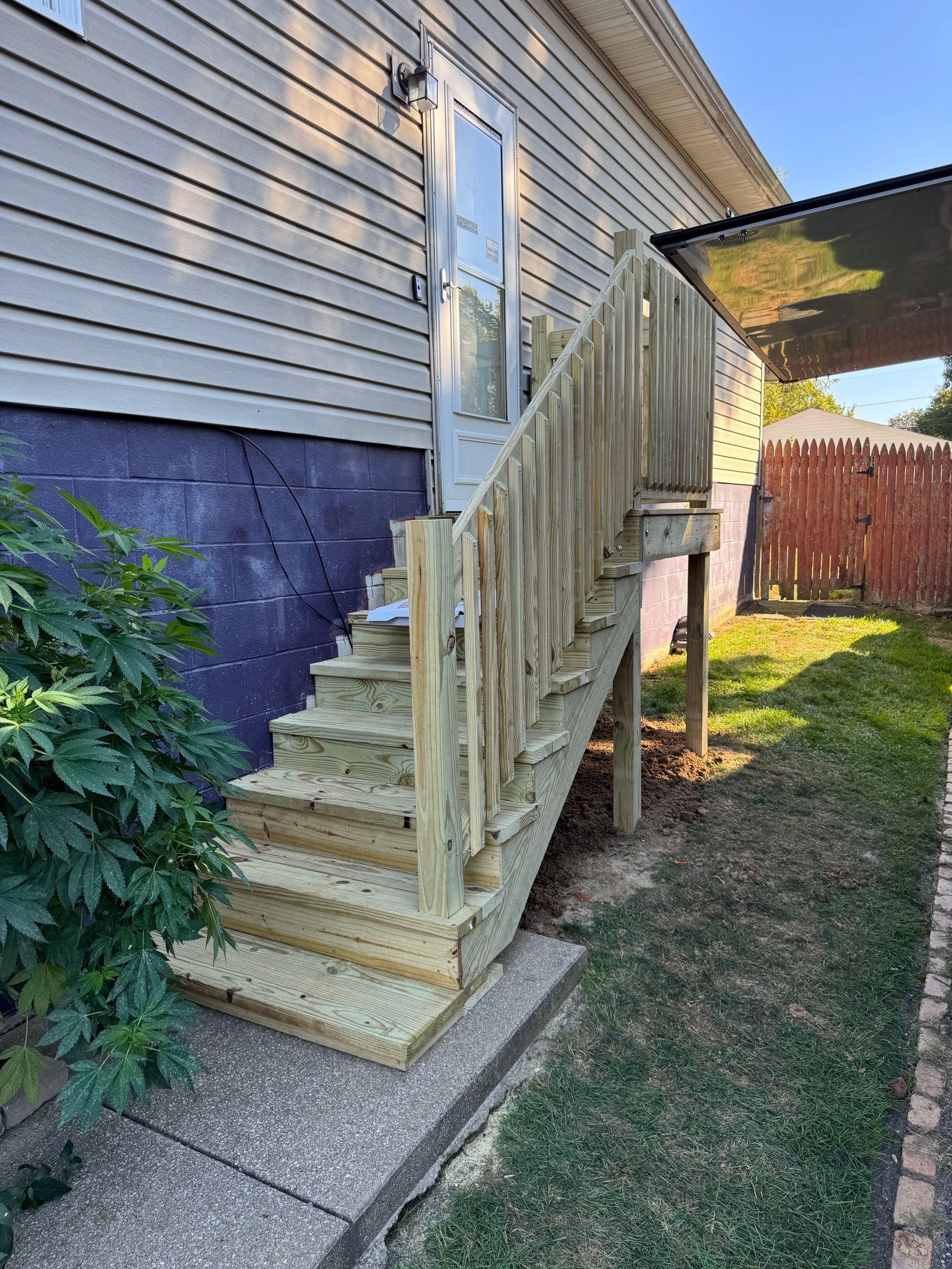 Exterior wooden stairs leading to a back door. The stairs have a railing and are next to a yard.
