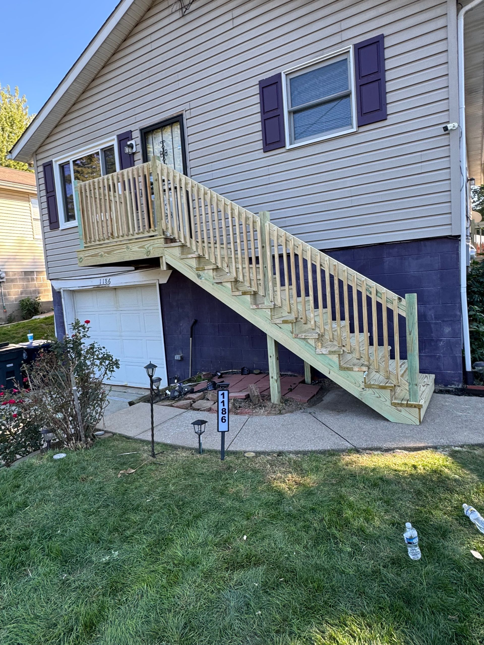 Wooden staircase leading up to a house with purple shutters. The house has light siding and a garage door.