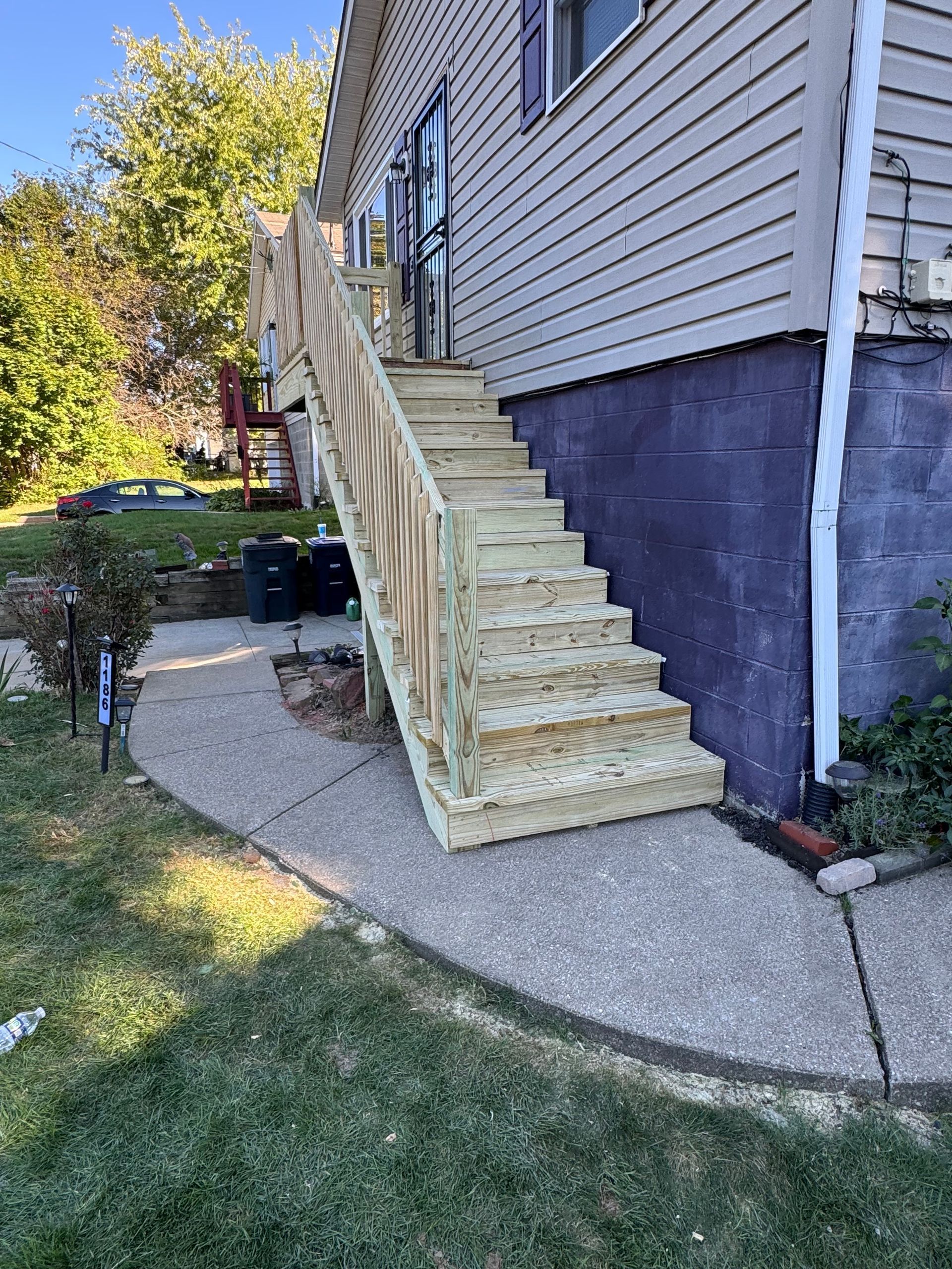 Wooden staircase leading up to a house entrance; concrete pathway in foreground.