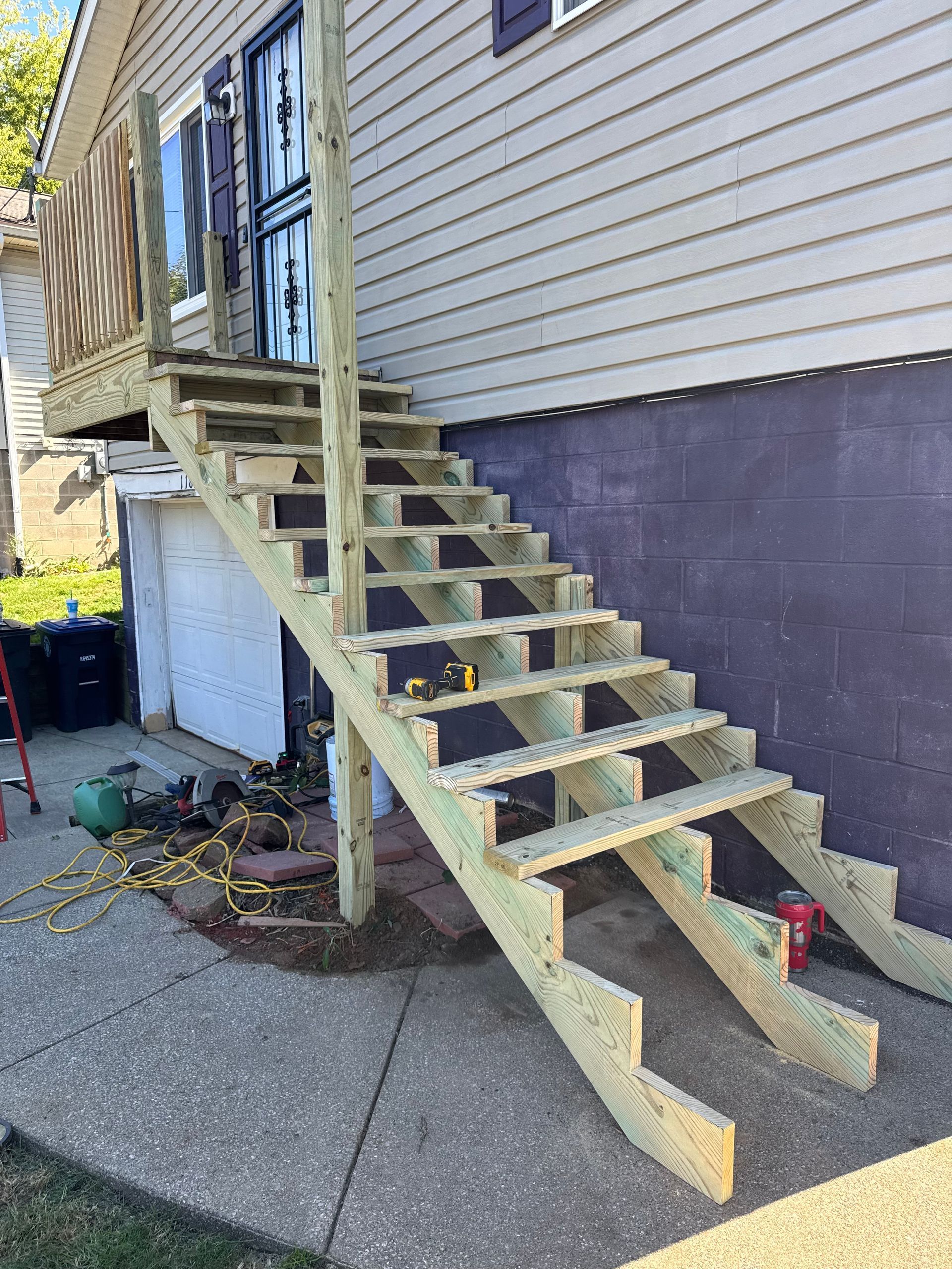 Wooden outdoor staircase leading to a porch and door on a house with gray siding.
