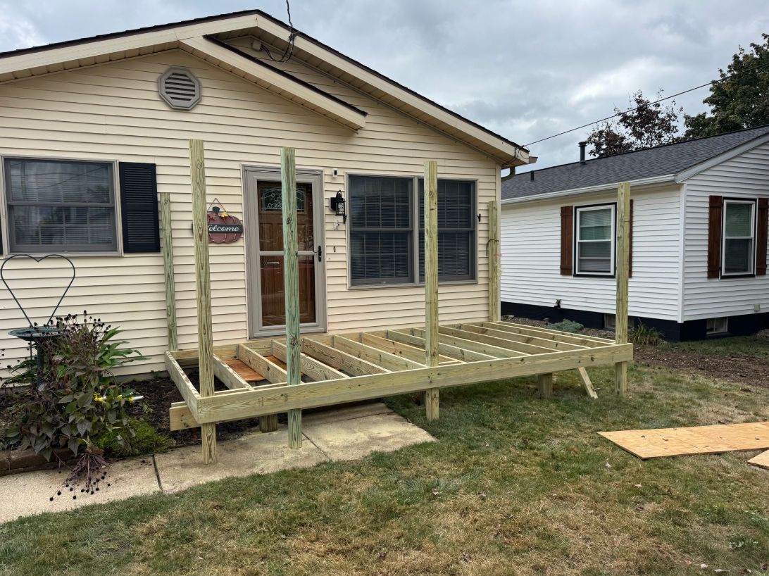 A partially constructed wooden deck in front of a beige house.