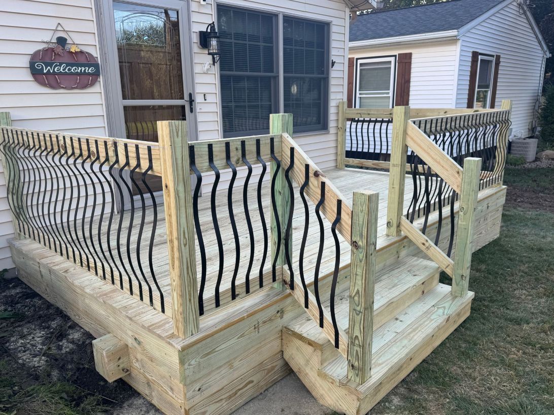 Wooden deck with steps and ornate black metal railing outside a house.