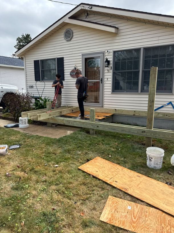 Two men building a wooden ramp in front of a white house with a glass door.