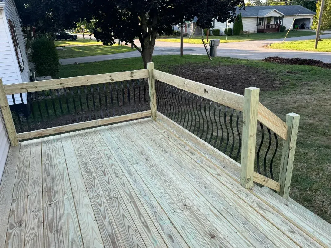 Wooden deck with black metal railings, a grassy yard, and houses in the background.