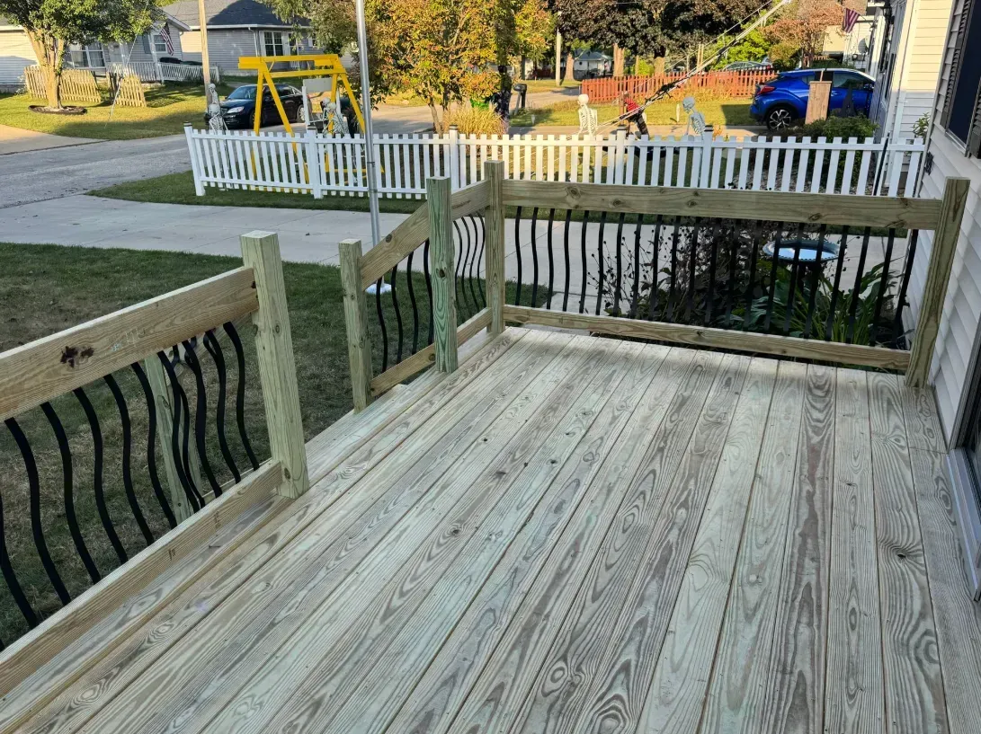 Wooden deck with black metal railings and a white picket fence in the background.