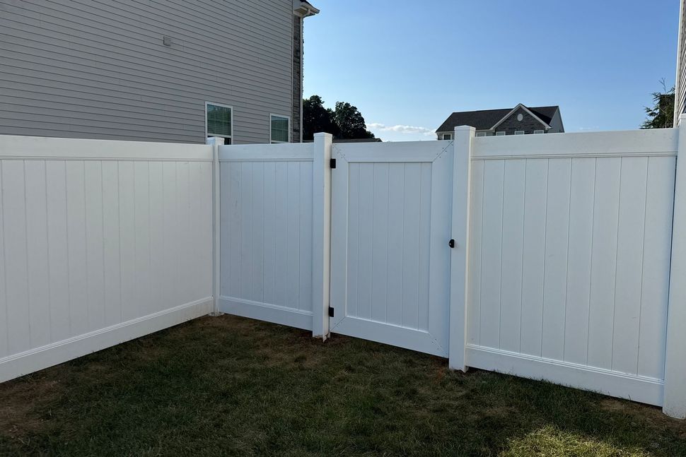White vinyl fence with gate in a backyard; grass in foreground, house in background.
