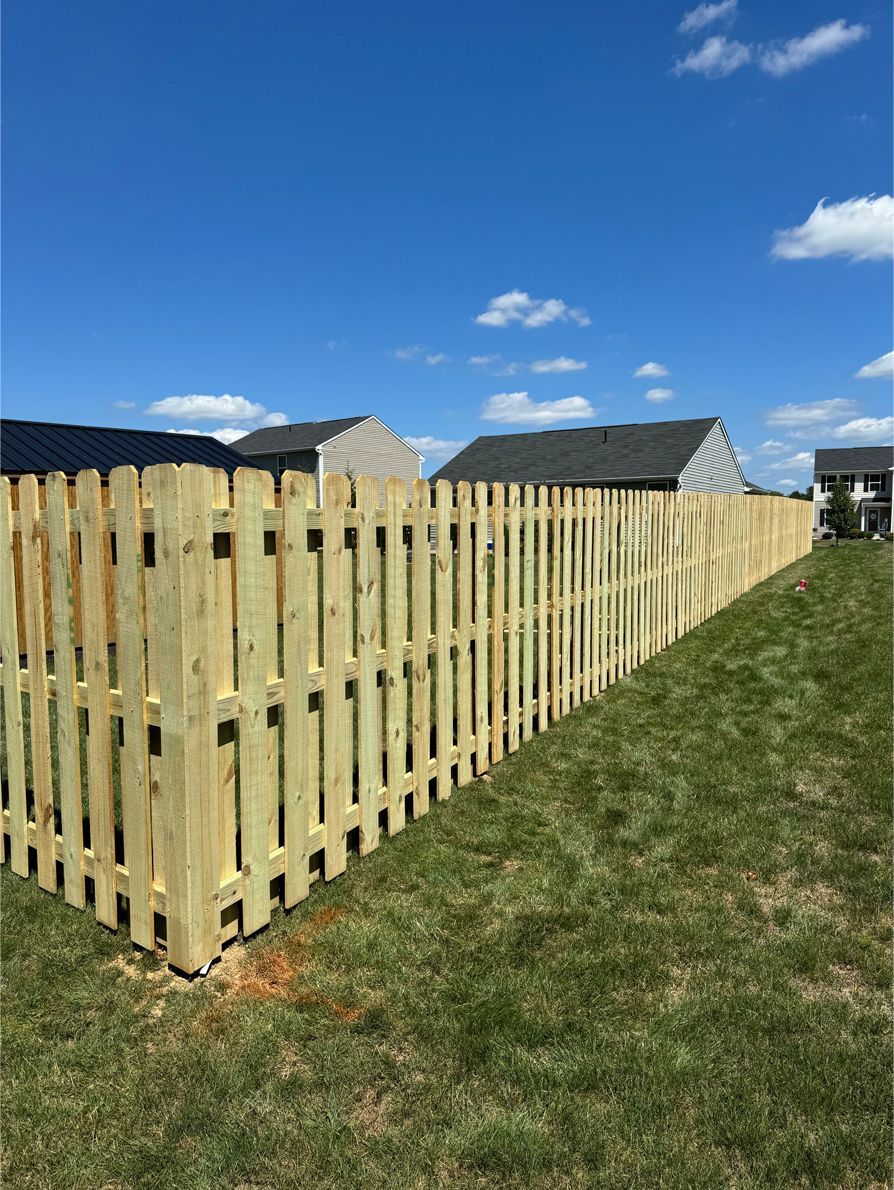 Wooden picket fence in a grassy yard under a blue sky with some houses in the background.