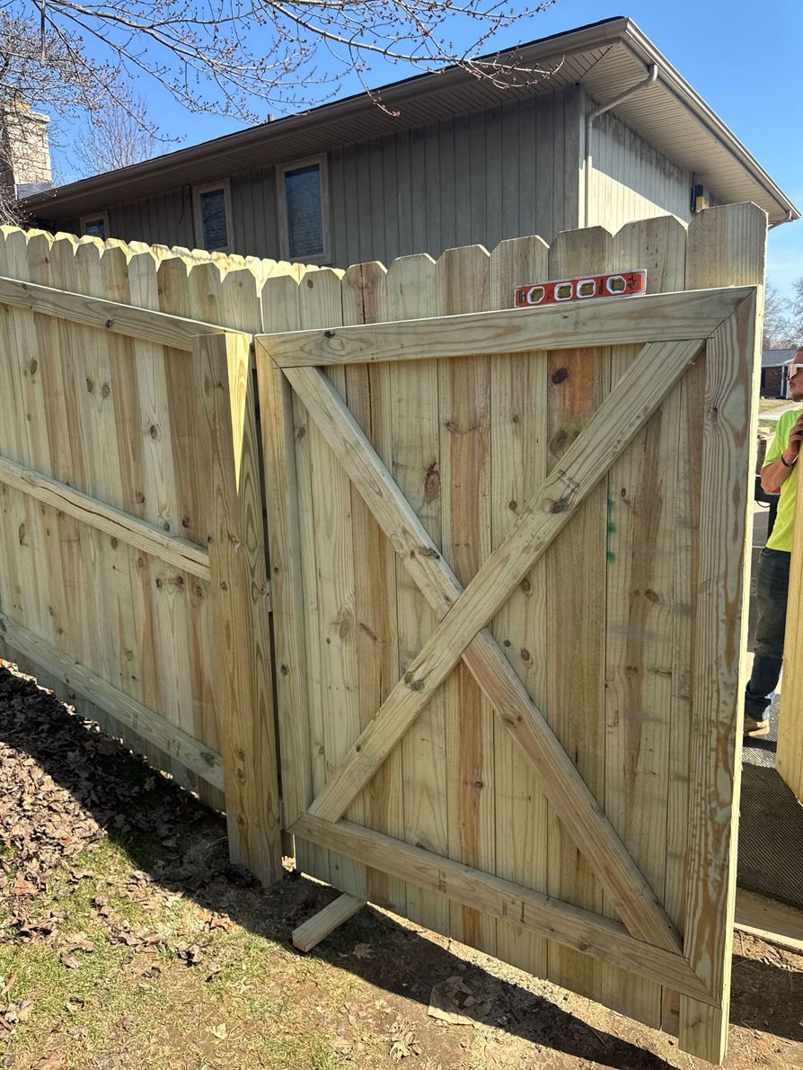 Wooden fence with gate, X-braced, in front of a house on a sunny day.