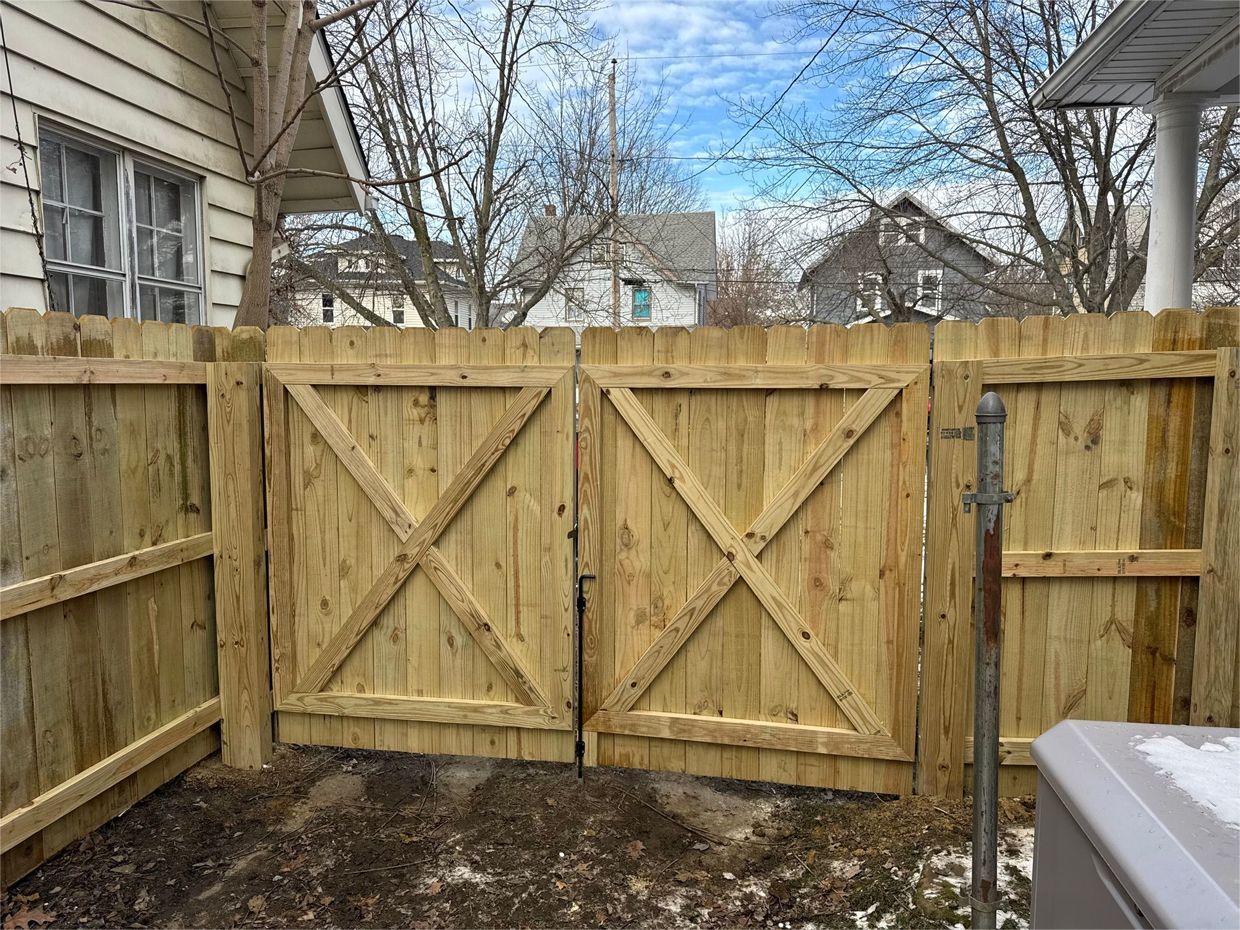 Wooden fence with double gate, outdoors. X-braced gate design, set against a cloudy sky.