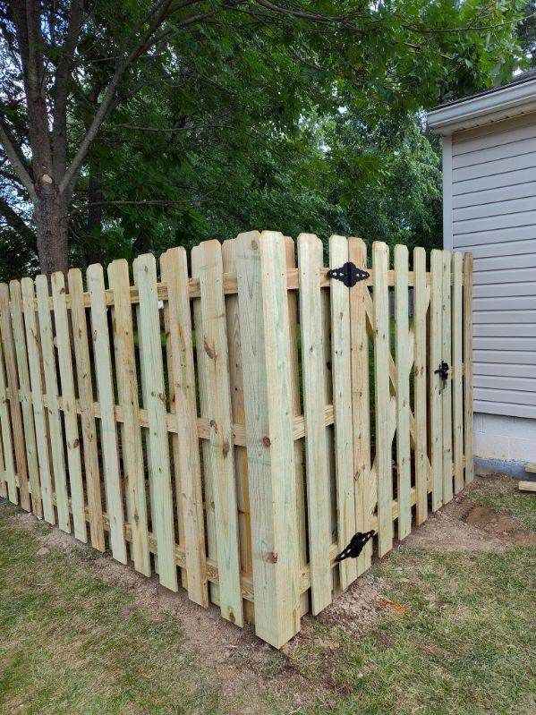 Wooden fence with a gate around a corner, near a tree and a building.