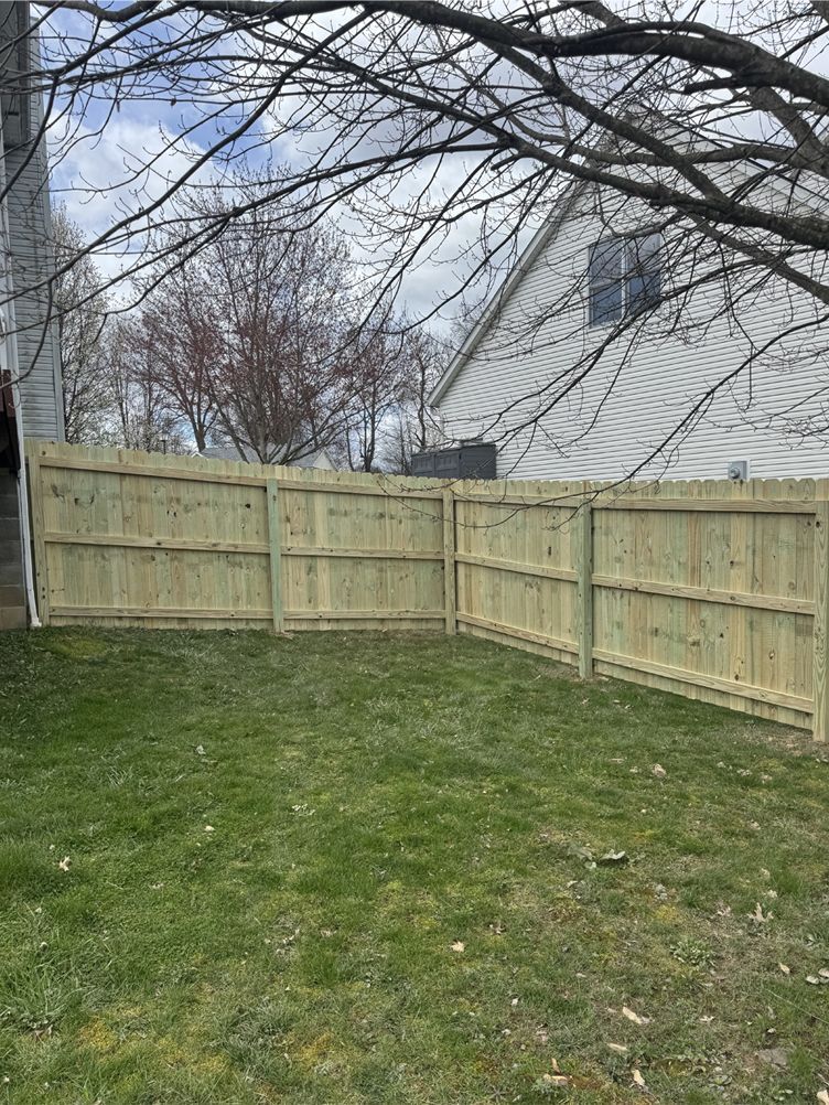 A newly built wooden fence encloses a grassy backyard, with a house and tree visible in the background.