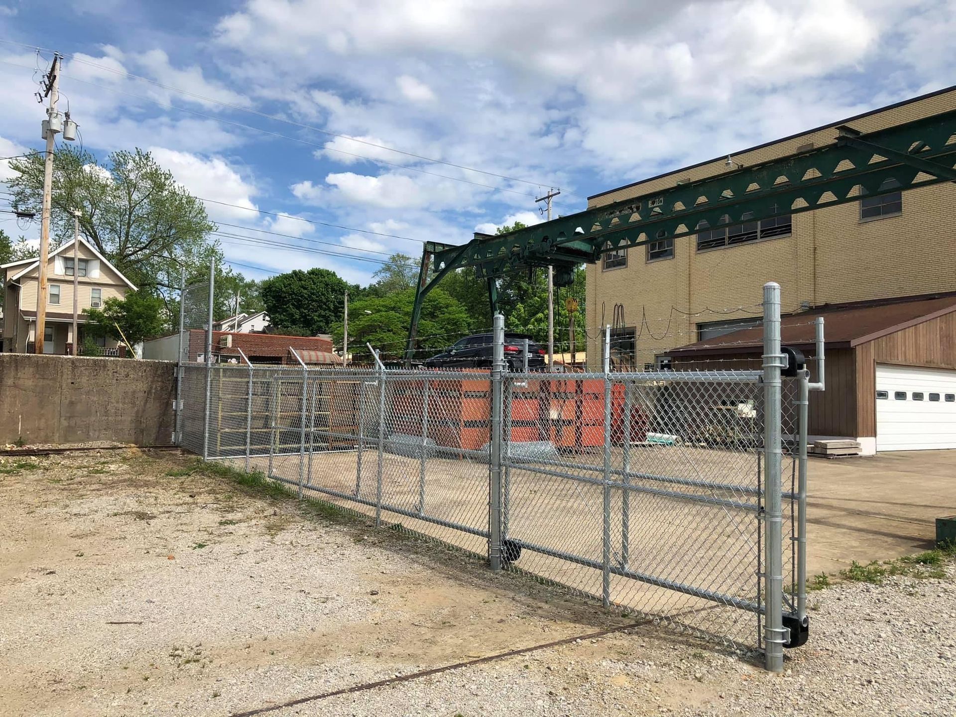 A chain-link fence with a gate surrounds a gravel lot. A large building is in the background.