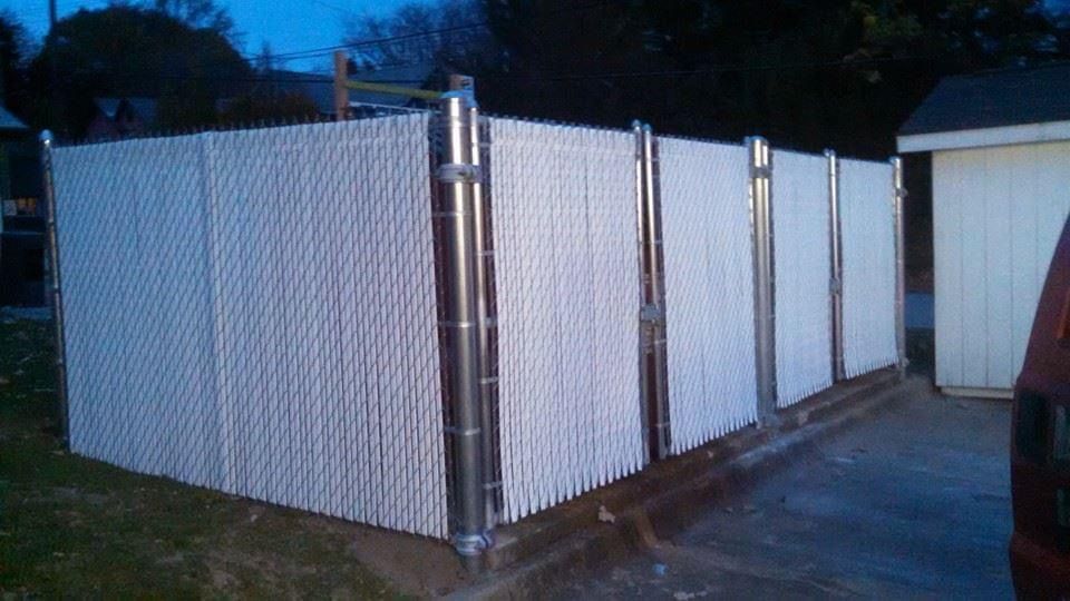 White vinyl slat privacy fence. Stainless steel posts.  Part of a house and a vehicle are visible.