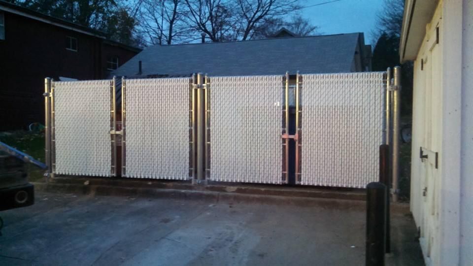 Chain link fence with white privacy slats, open gate in front of building.