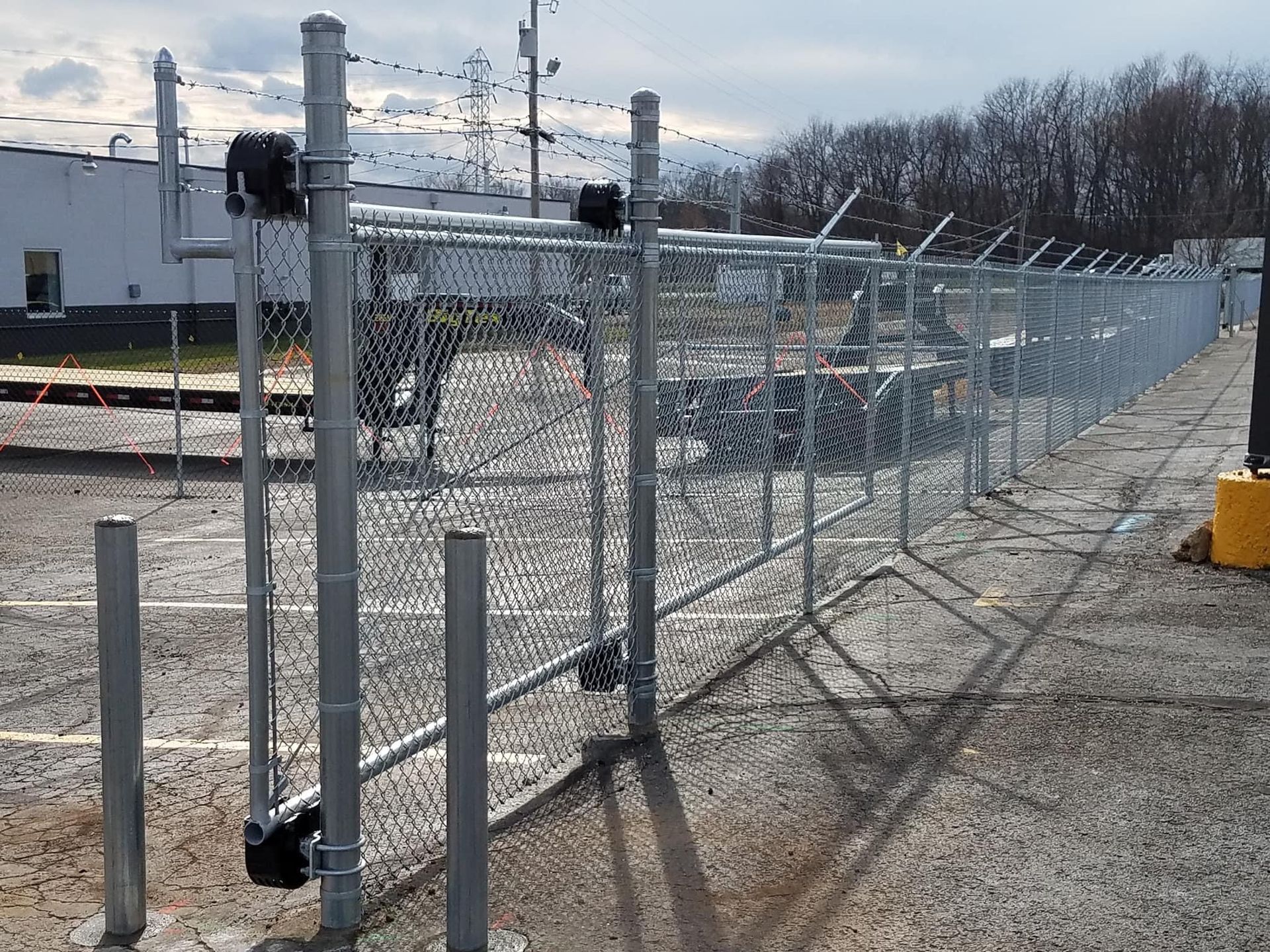 Chain-link fence with barbed wire, a gate, and posts in a paved industrial area.