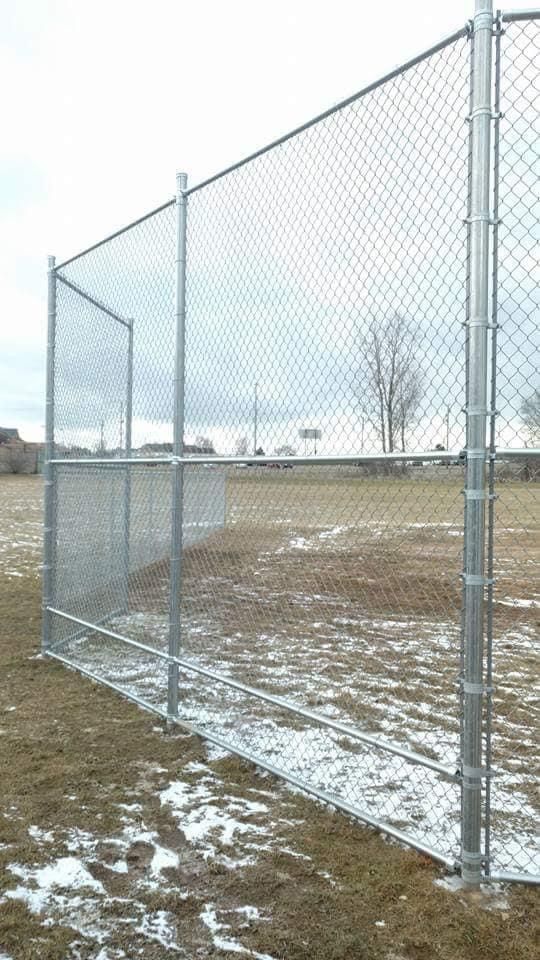 Chain-link fence on a grassy field under a cloudy sky.
