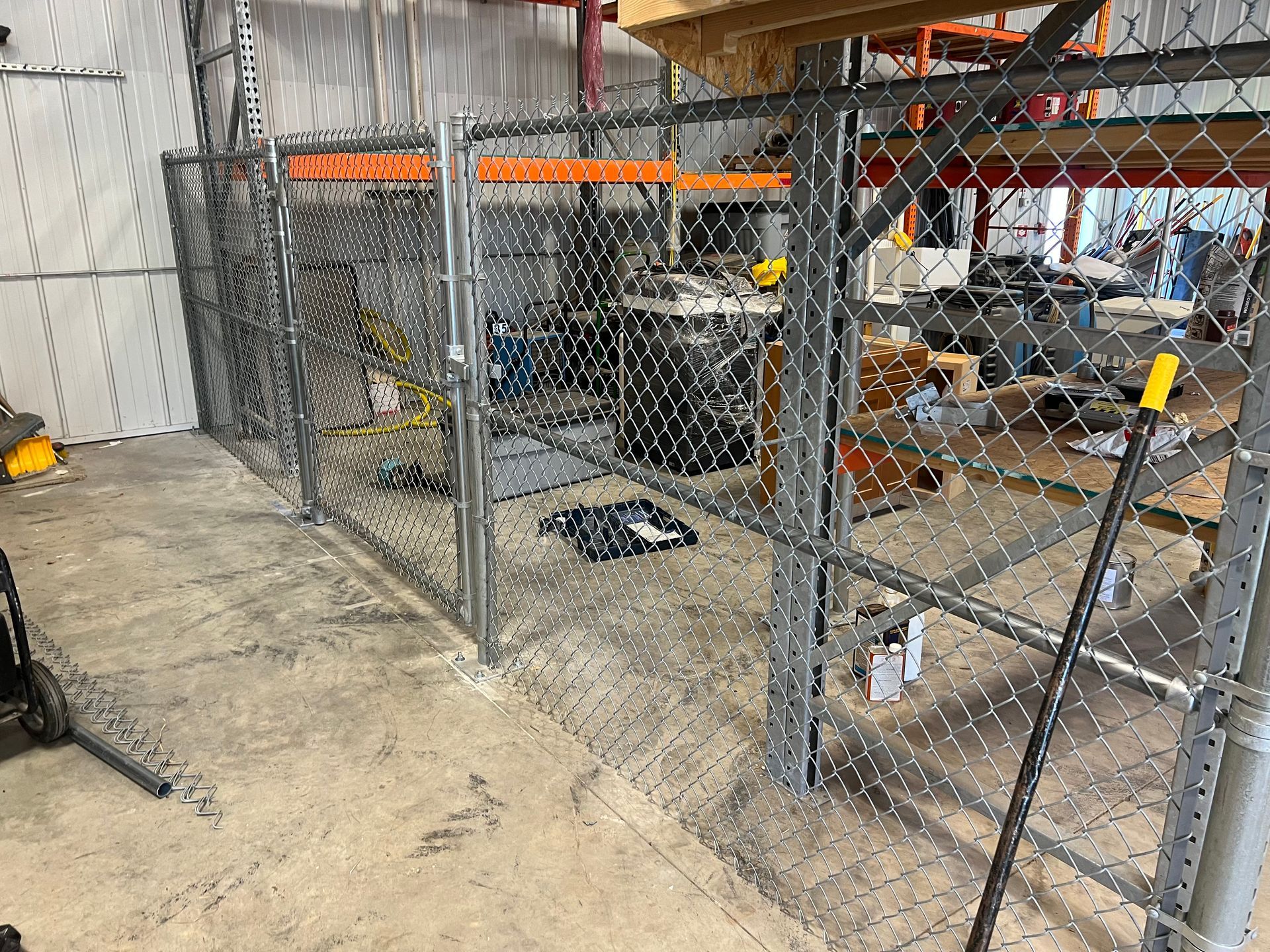 Chain-link fence enclosure inside a warehouse; gray, open gate; concrete floor.