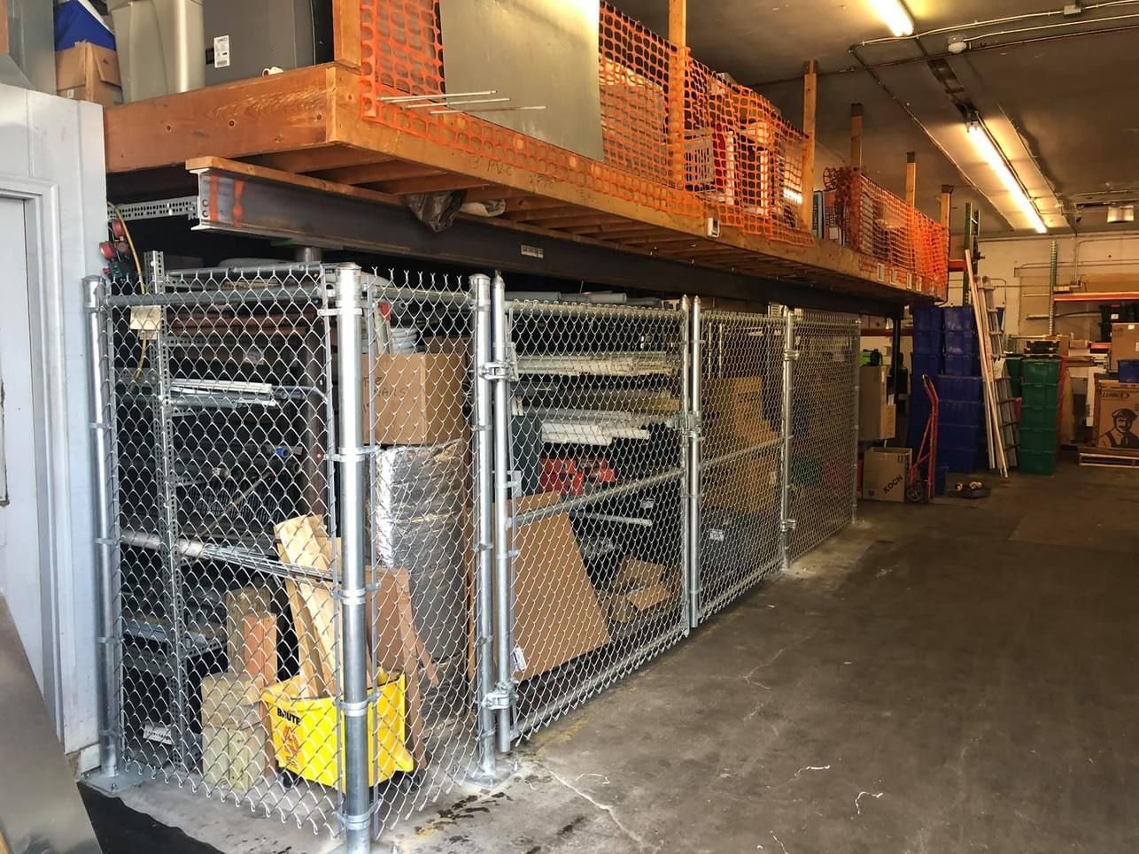 Warehouse storage: Metal cages beneath a wooden loft, holding tools and supplies.