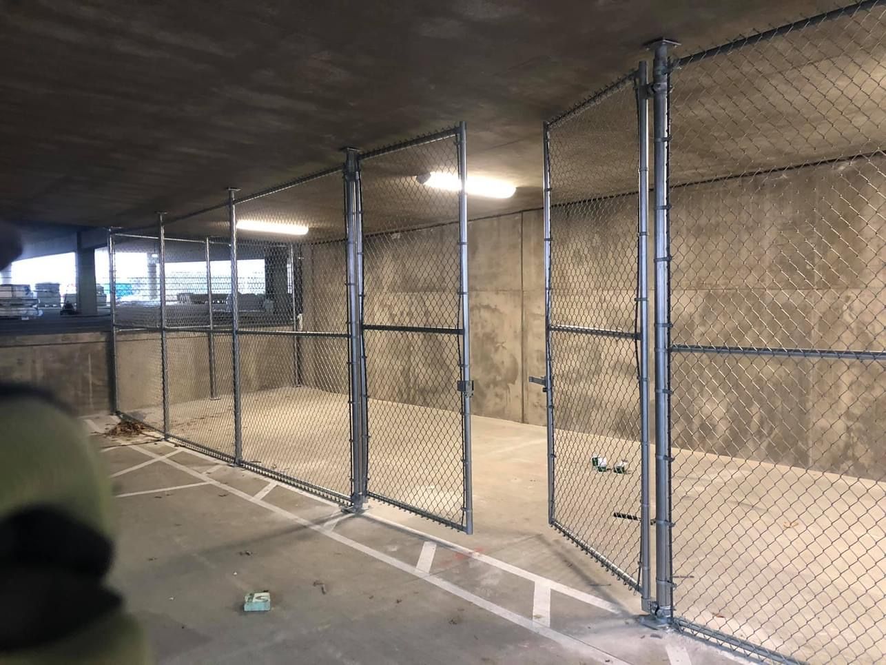 Chain-link fenced storage units under concrete ceiling.