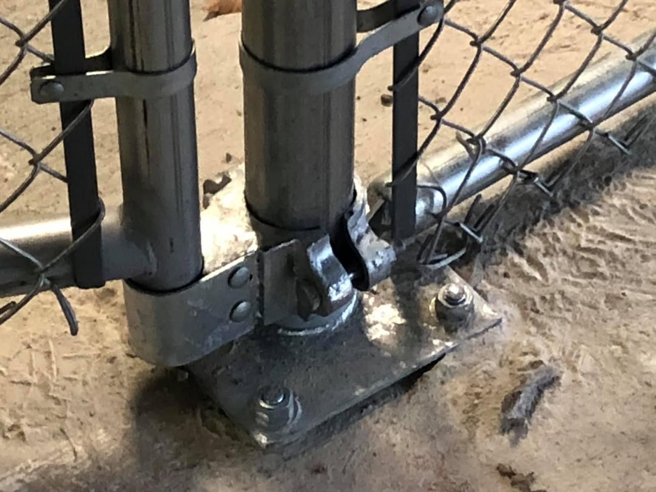 Chain link fence post secured to a concrete base with metal brackets and bolts.