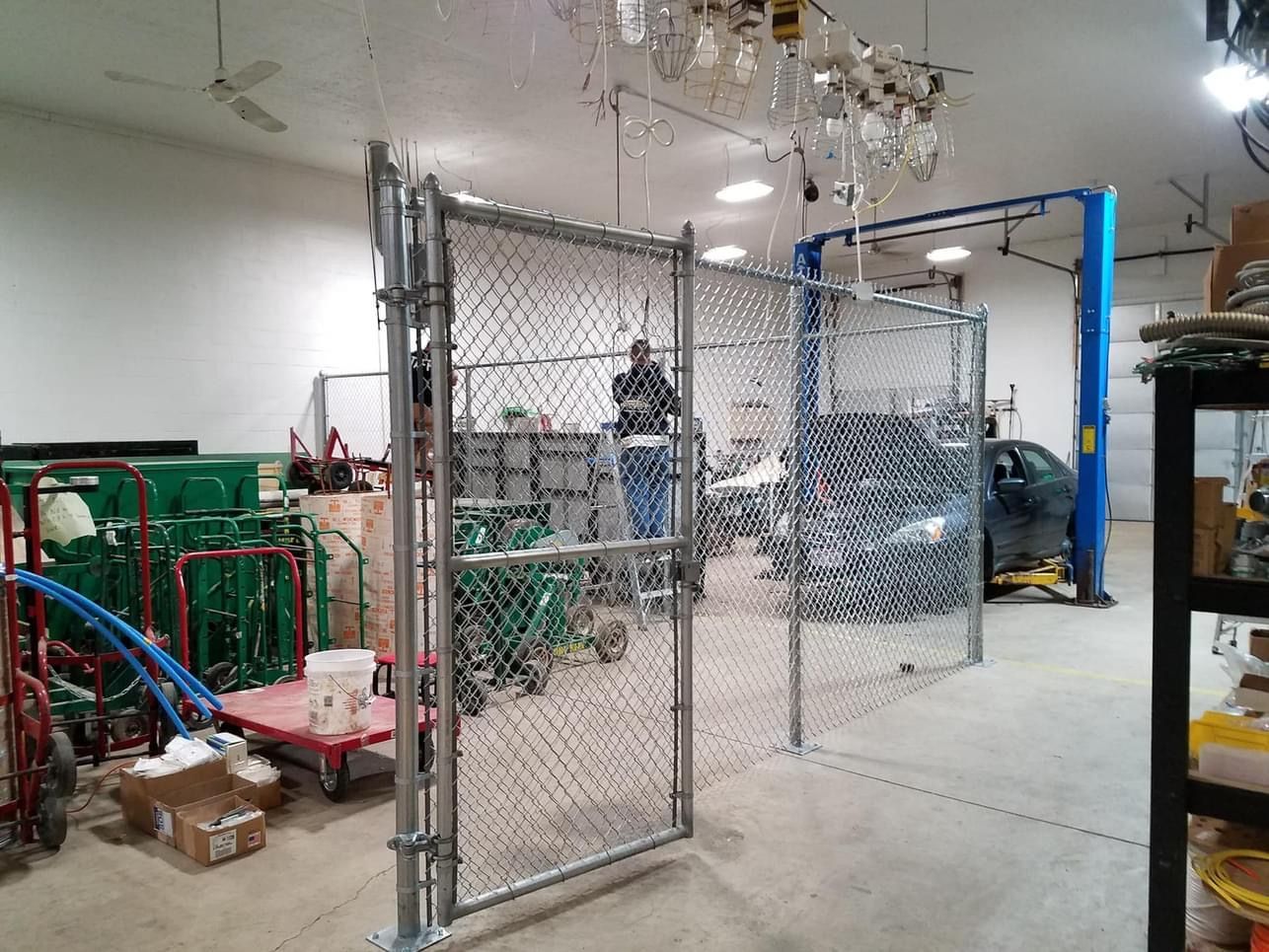 A chain-link fence partially encloses a garage area with a car lift and tools; a person is visible within.