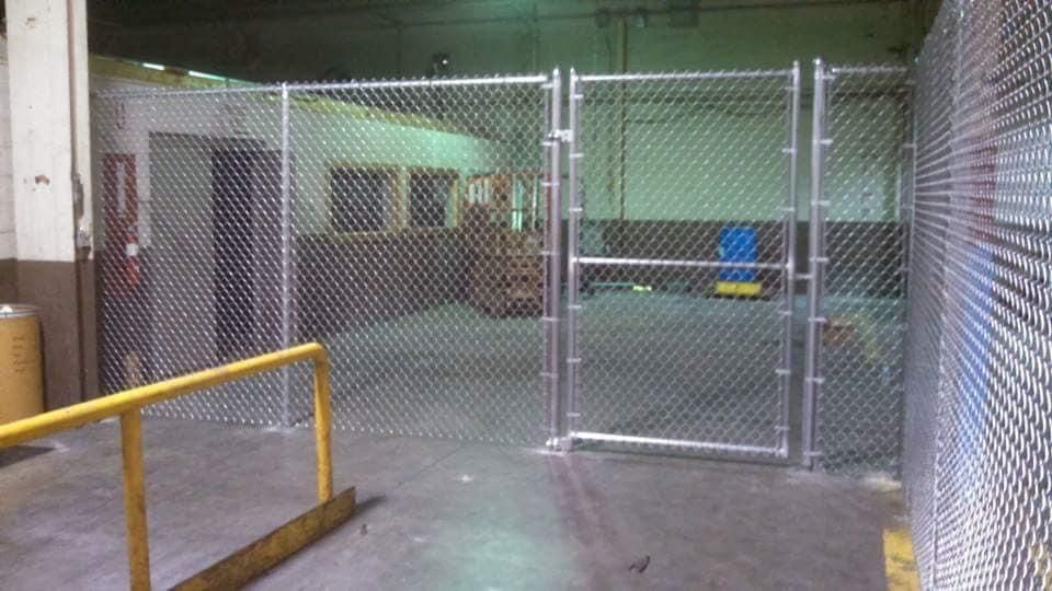 Metal chain link fence with a gate, in a warehouse setting.