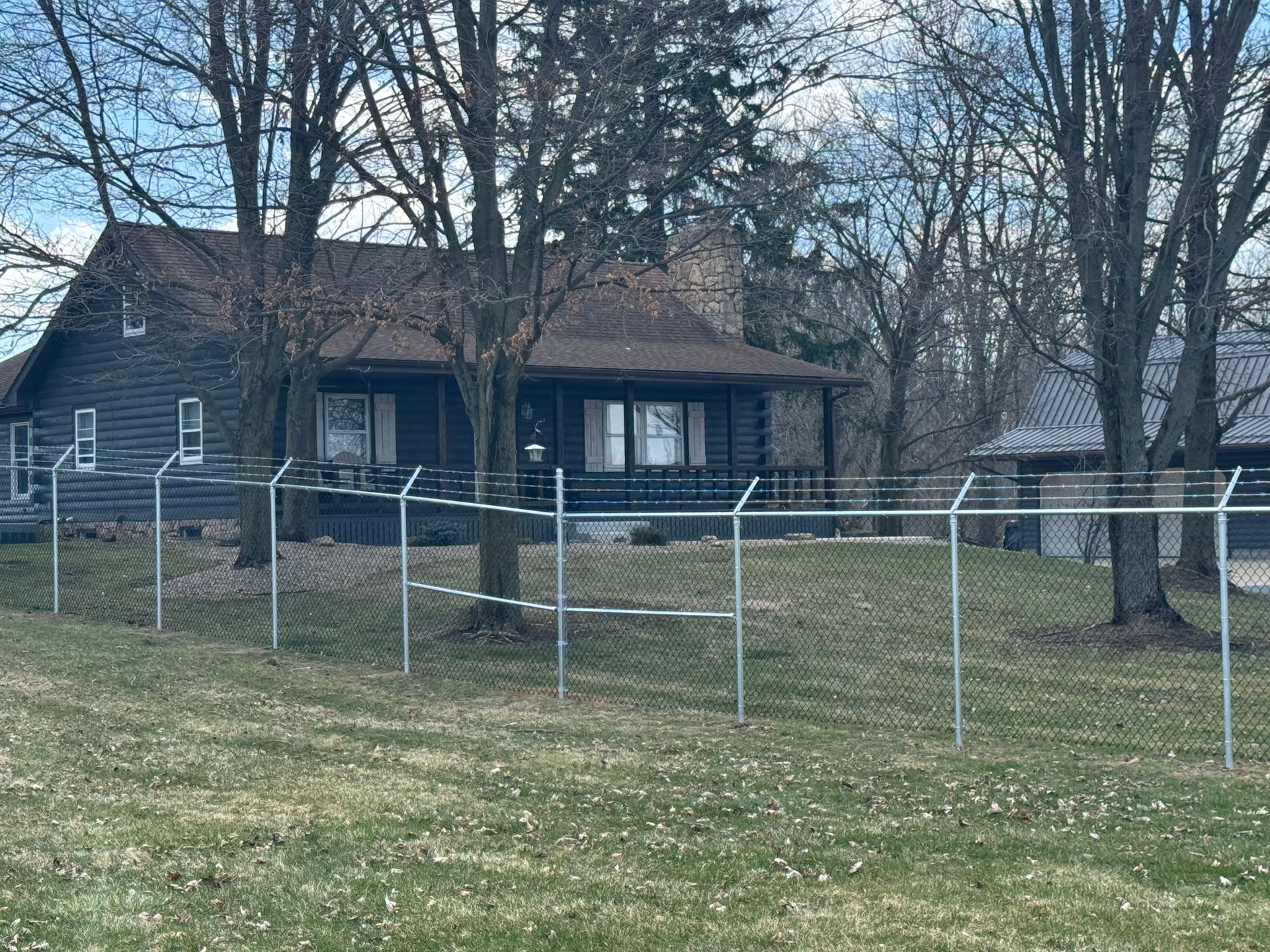 House with a chain-link fence in front, trees in the background, and a cloudy sky.