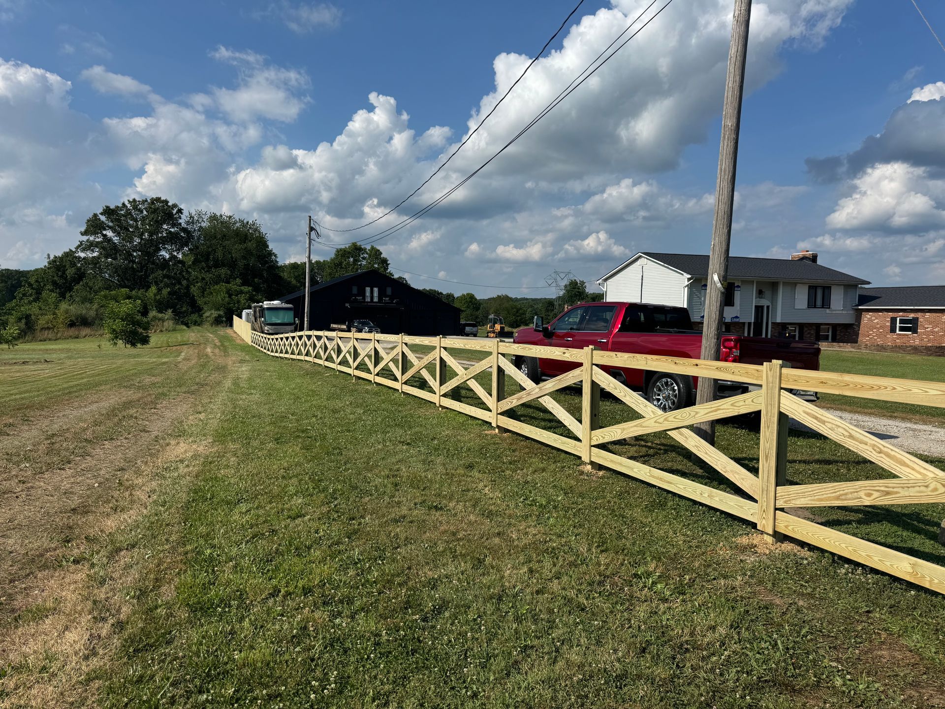 Wooden fence along a grassy field, red truck, black house, and blue sky.