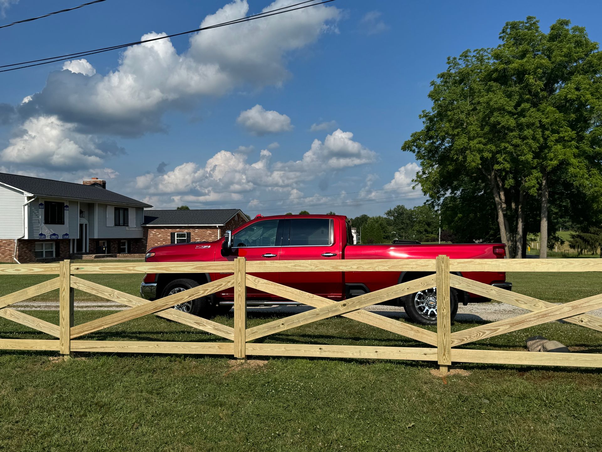 Red pickup truck behind a wooden fence in front of a house on a sunny day.
