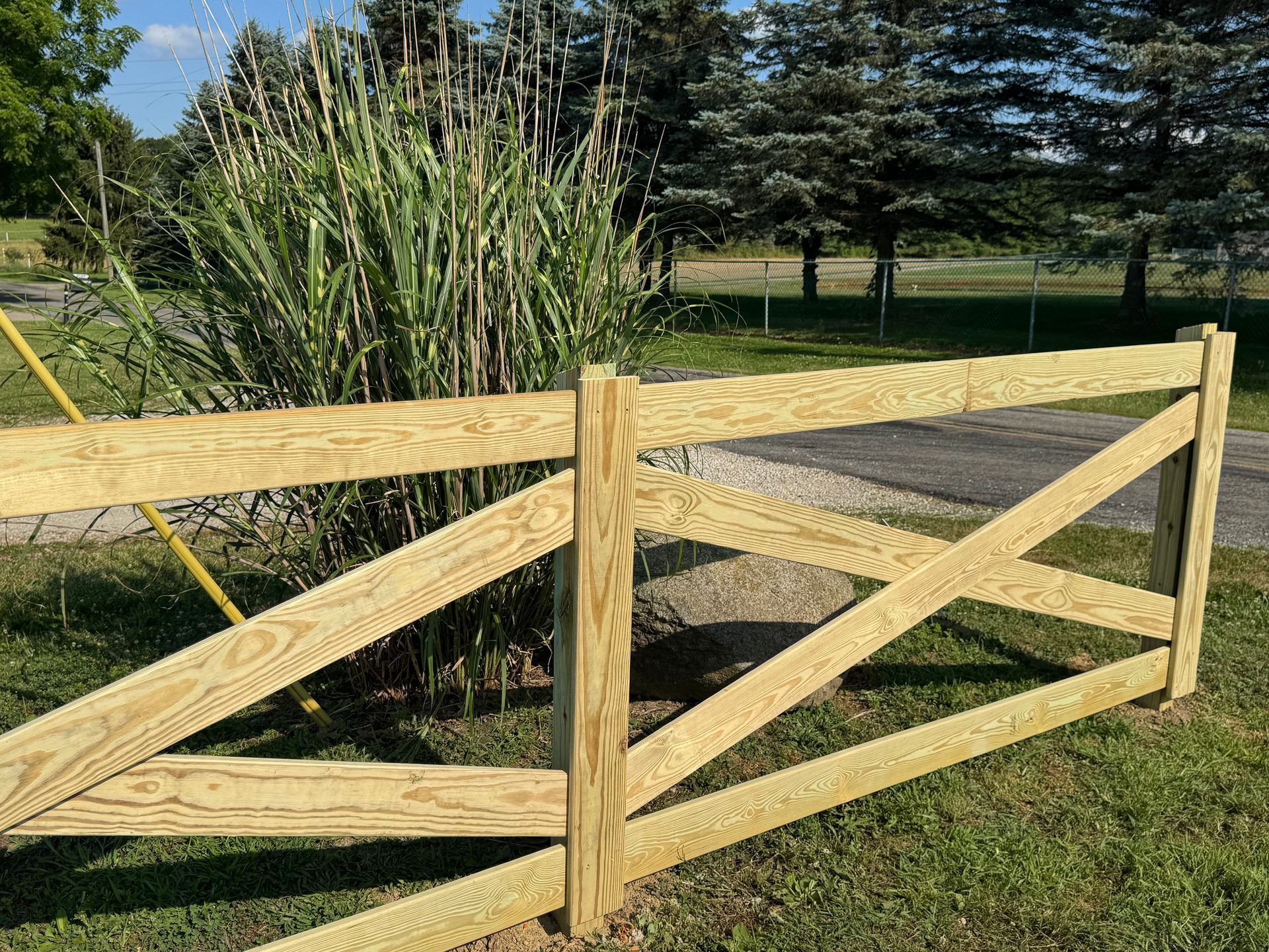 Wooden fence with an X-shaped pattern, in front of tall grass and trees.