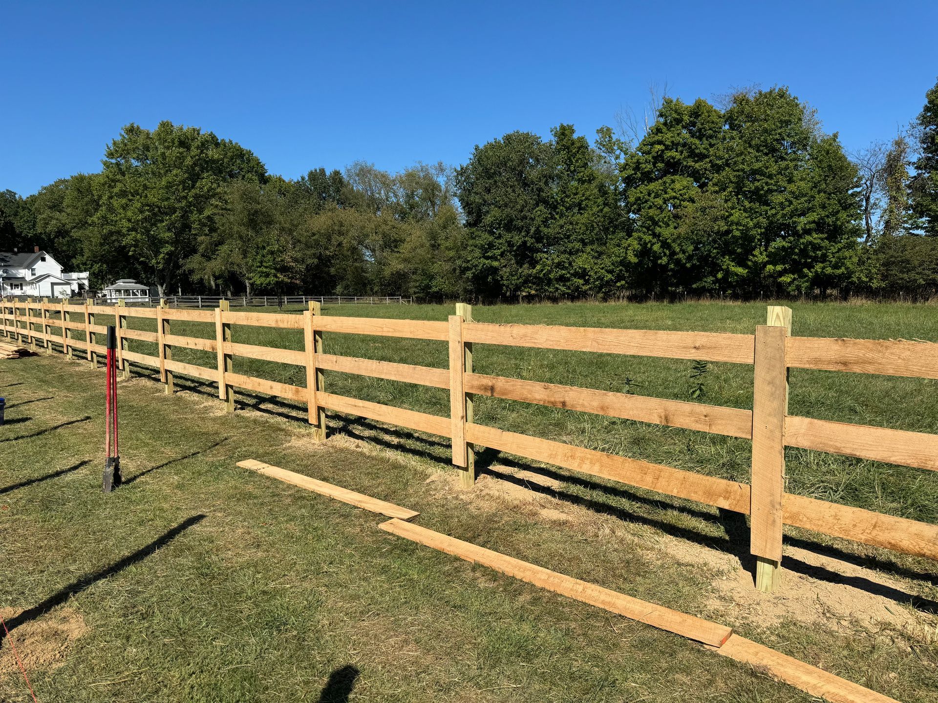 Wooden split-rail fence being constructed in a grassy field under a clear blue sky.