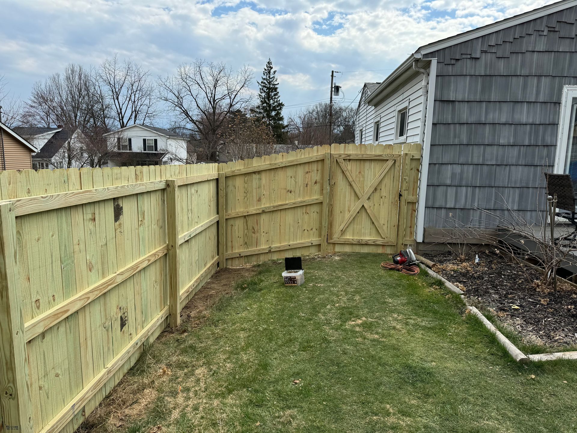 A wooden fence encloses a grassy backyard, with a gate and house visible.