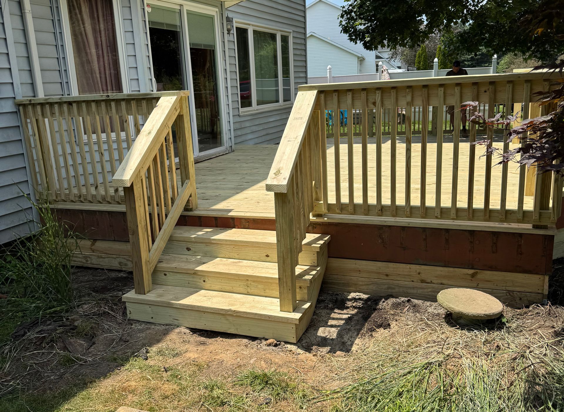 Wooden deck with stairs and railing outside a gray house.