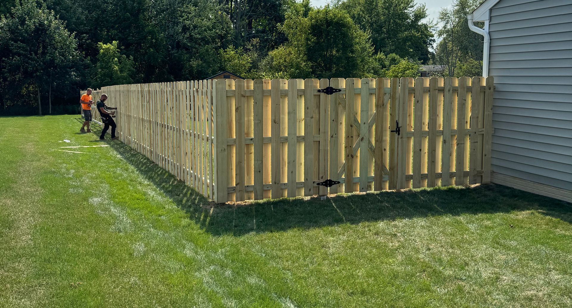 Wooden picket fence enclosing a backyard with two people working on the left side.