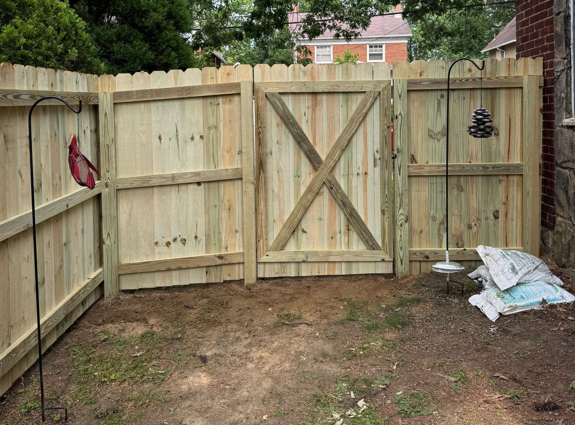 Wooden fence with a gate in a backyard. Bird feeders hang from poles.