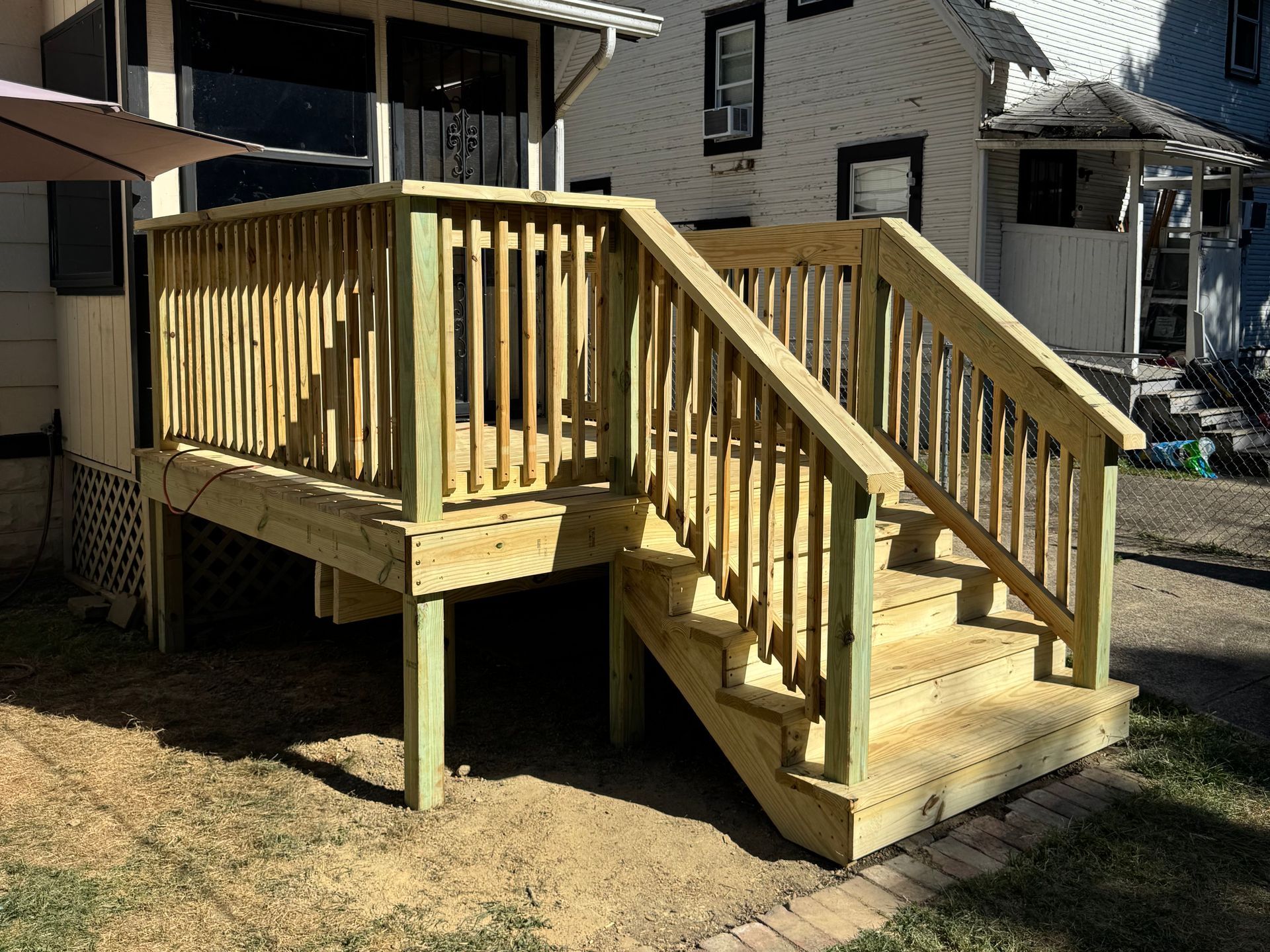 Wooden deck with railing and stairs; outdoors with house in background.