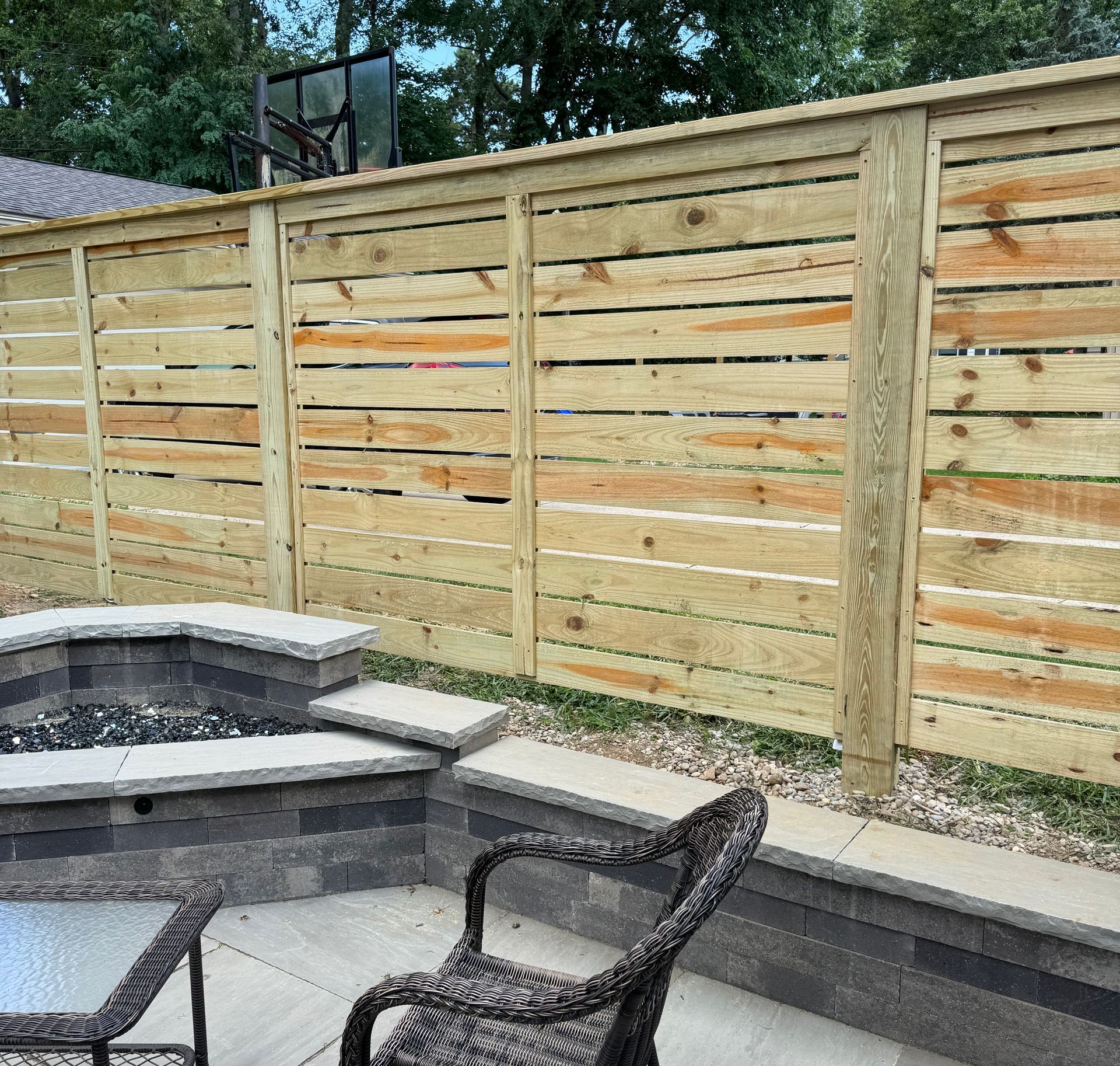 Wooden slat fence behind a patio with fire pit, seating.